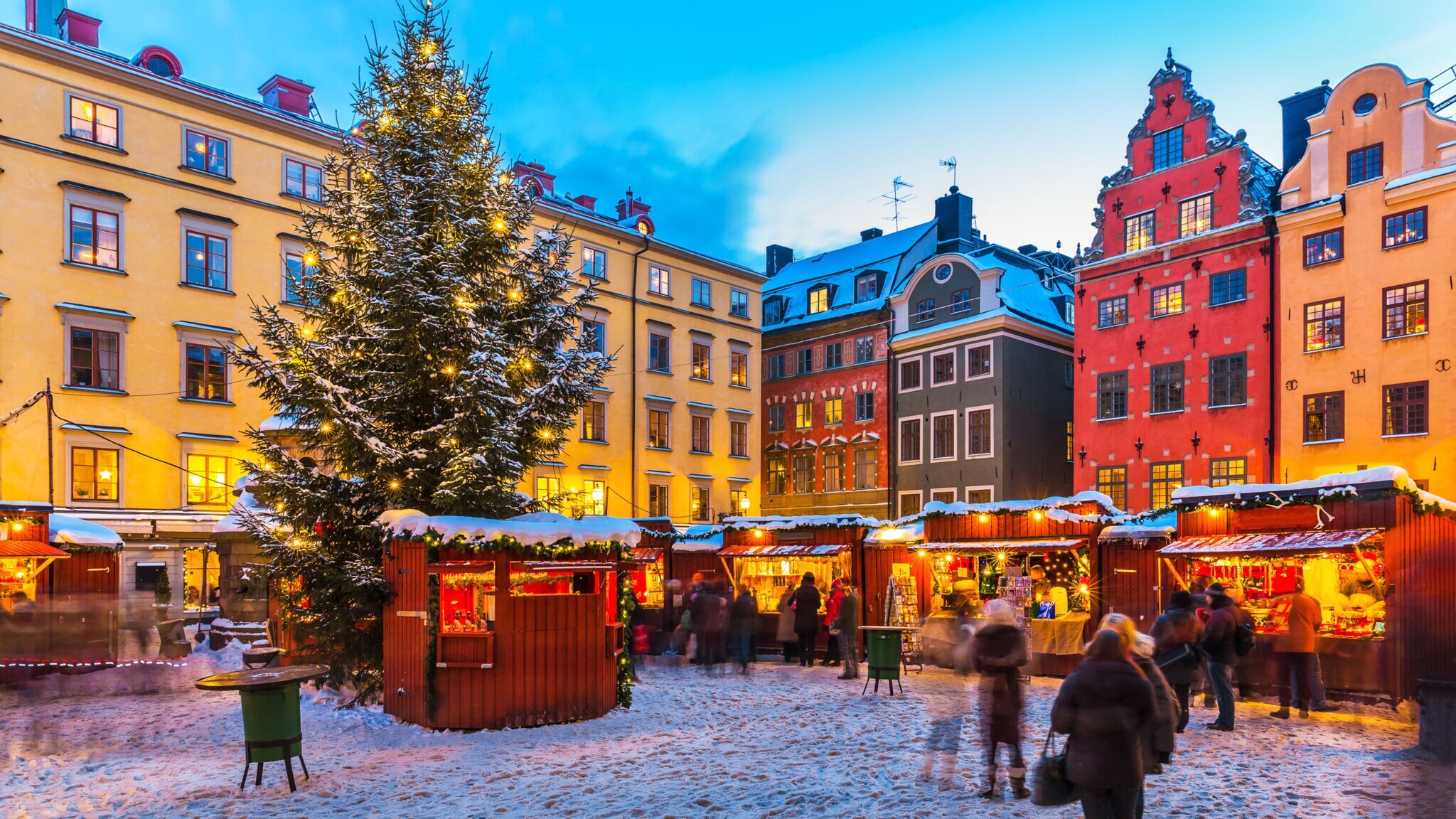 Weihnachtsmarkt auf einem Platz in der Altstadt von Stockholm mit vielen Ständen, Schnee und einem Tannenbaum.