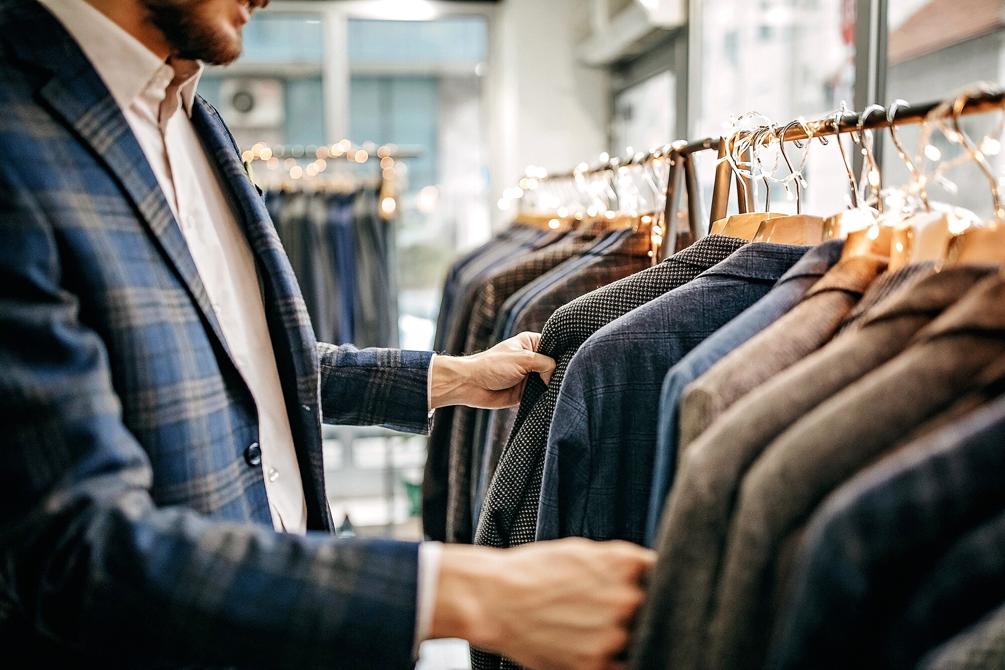 Die 3 wichtigsten Business-Dresscodes: Dein Styleguide zum Erfolg. Ein Mann steht in einer Boutique und wählt ein passendes Sakko aus.