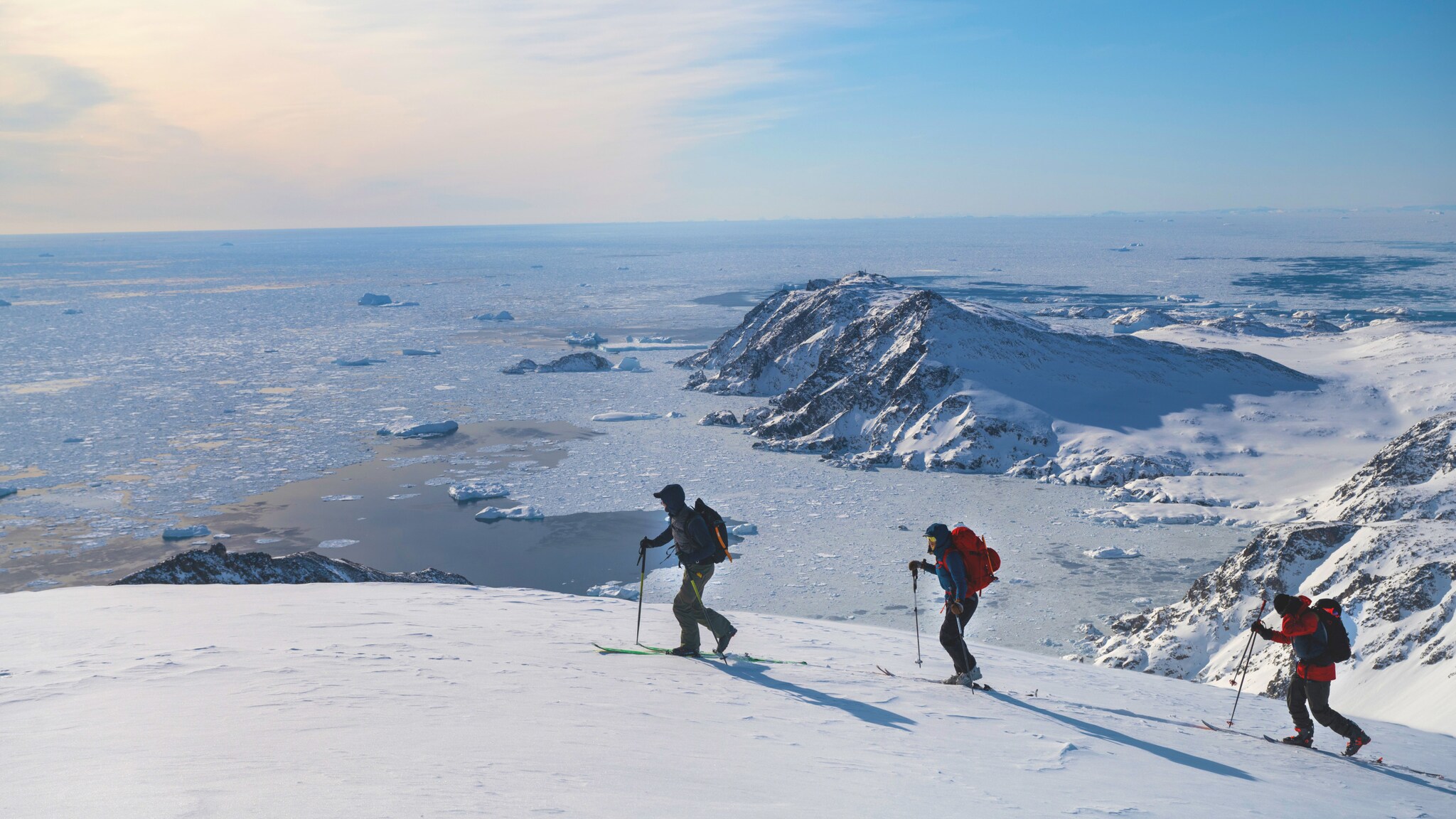 Drei Personen auf Skiern laufen einen schneebedeckten Bergkamm vor einer Gletscherlandschaft entlang. Drei Personen auf Skiern laufen einen schneebedeckten Bergkamm vor einer Gletscherlandschaft entlang.
