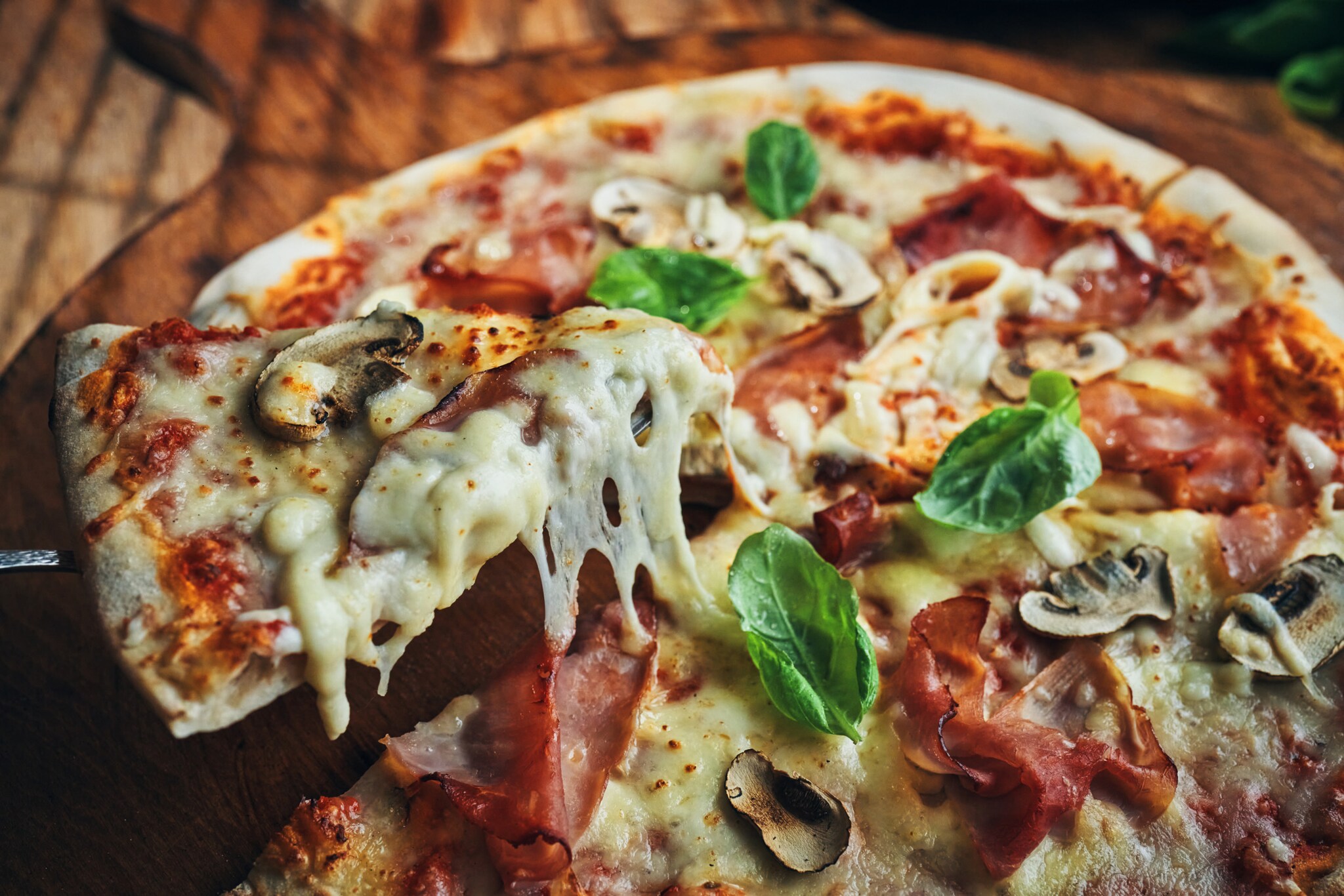 Nahaufnahme einer Pizza mit Champignons, Schinken und Basilikum auf zerlaufenem Käse.