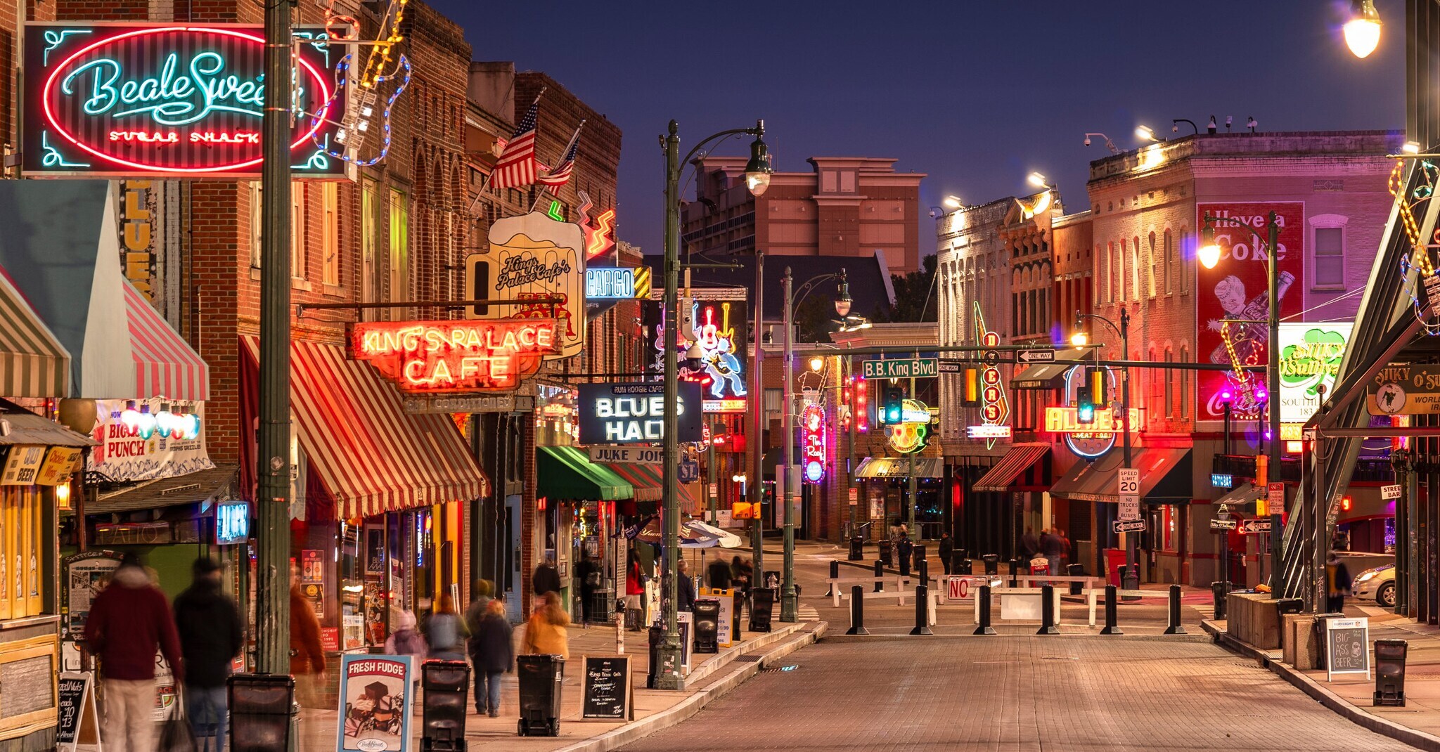 Autofreie Straße mit zahlreichen Bars mit beleuchteten Neonschildern bei Dunkelheit.