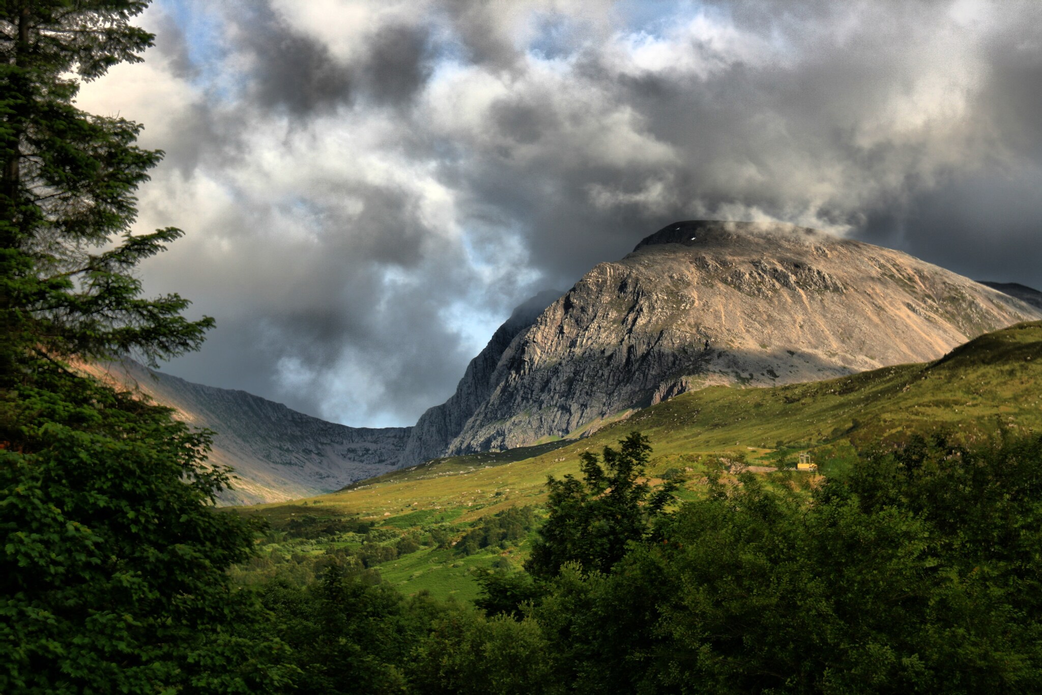 Blick auf den Berg Ben Nevis in Schottland bei stark bewölktem Himmel, im Vordergrund eine grüne Landschaft. Blick auf den Berg Ben Nevis in Schottland bei stark bewölktem Himmel, im Vordergrund eine grüne Landschaft.