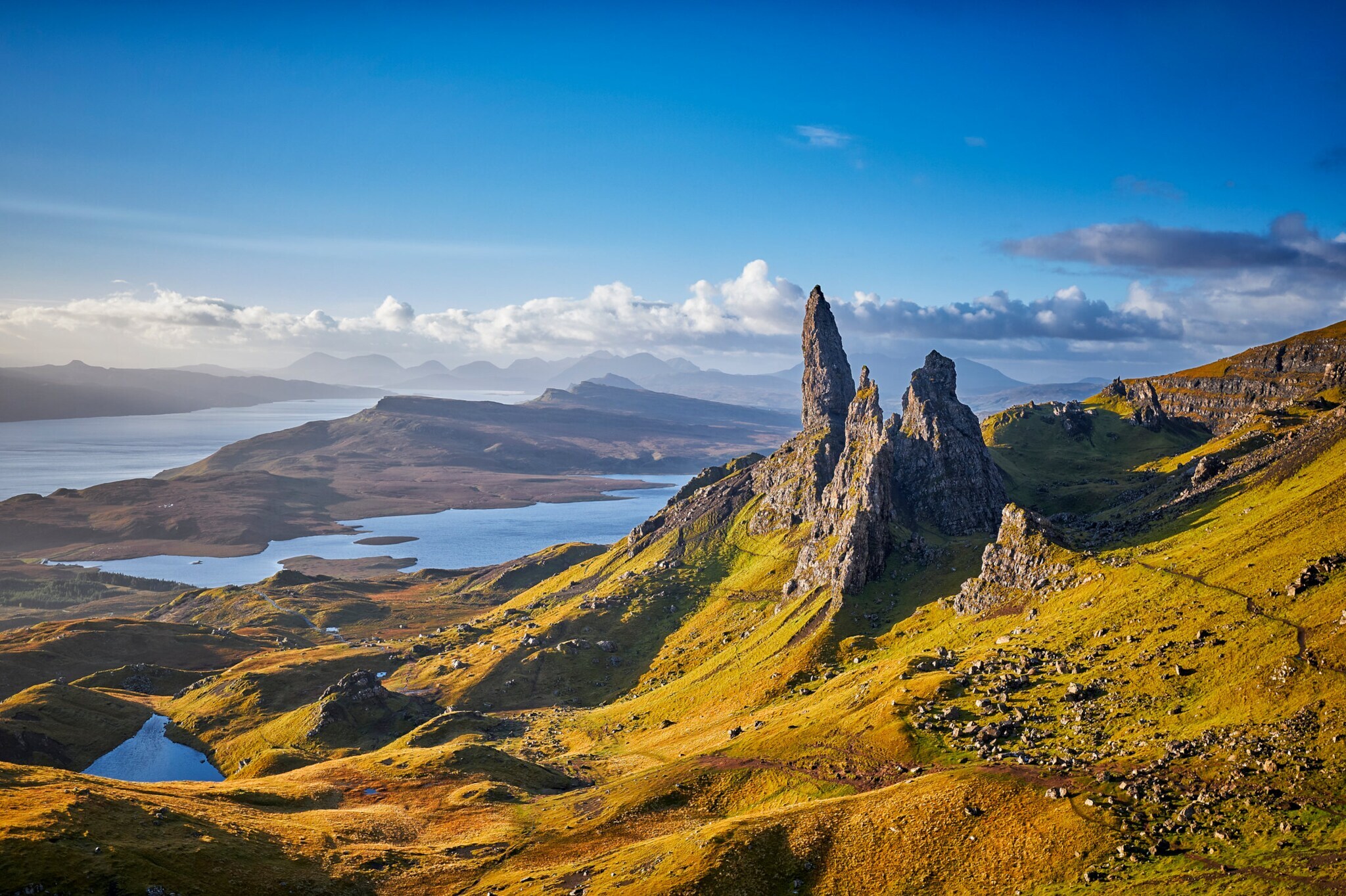 Blick auf den Old Man of Storr, ein markantes Felsmassiv, das von einer grünen Landschaft mit Seen umgeben ist. Blick auf den Old Man of Storr, ein markantes Felsmassiv, das von einer grünen Landschaft mit Seen umgeben ist.