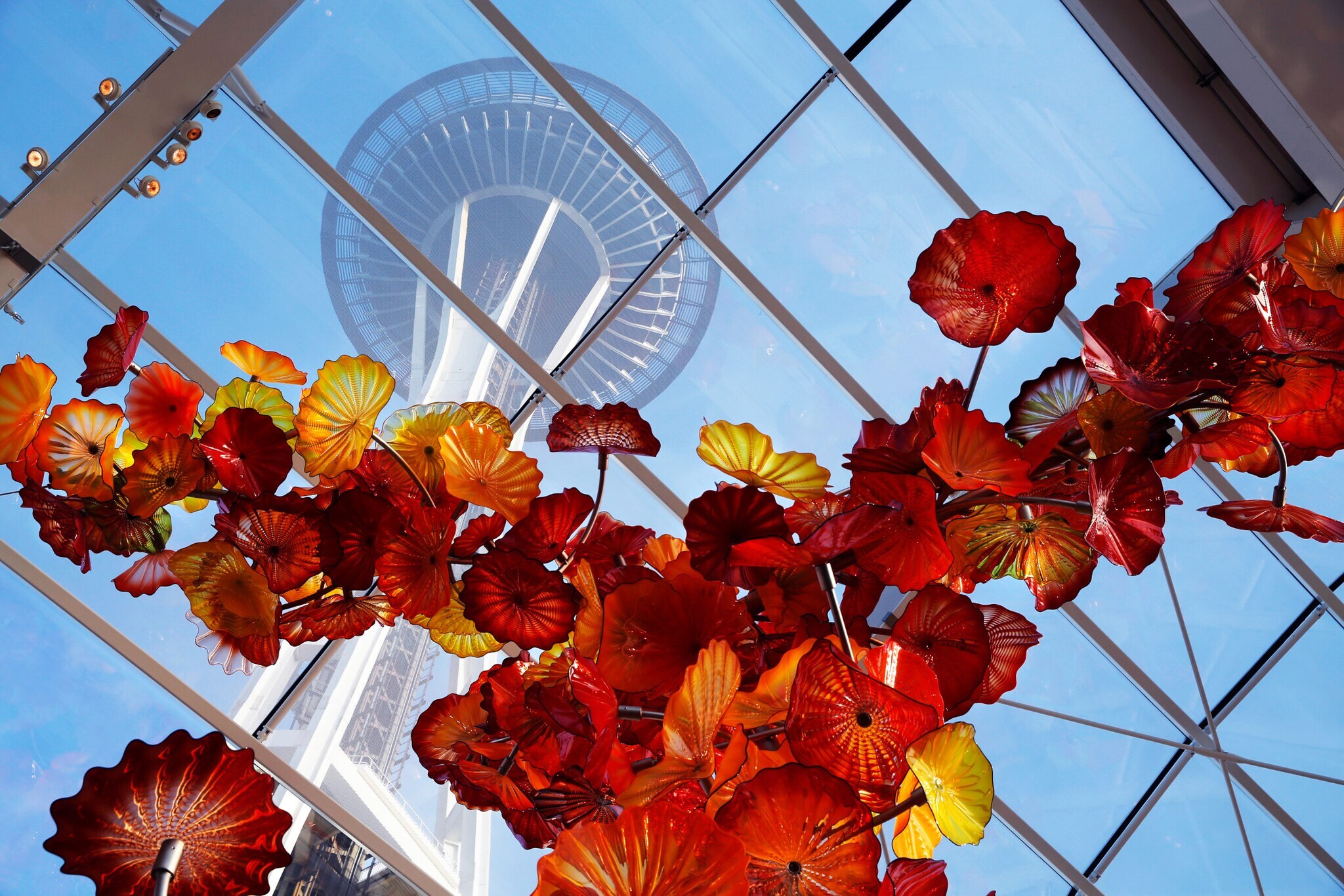 Untersicht einer Blumenglasskulptur in Rot- und Gelbtönen in einem Gebäude mit Glasdach unterhalb eines runden Turms.
