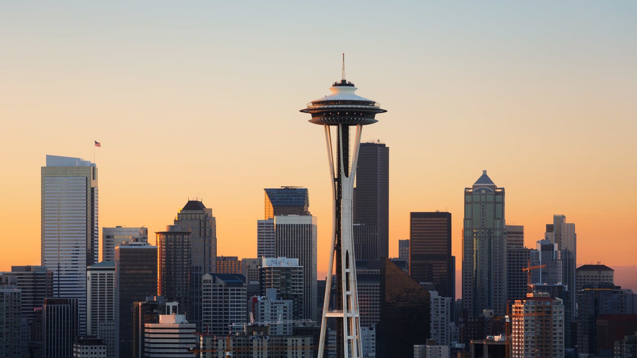 Skyline von Seattle mit Wolkenkratzern und rundem Space-Needle-Turm vor organge gefärbtem Himmel bei Sonnenuntergang.
