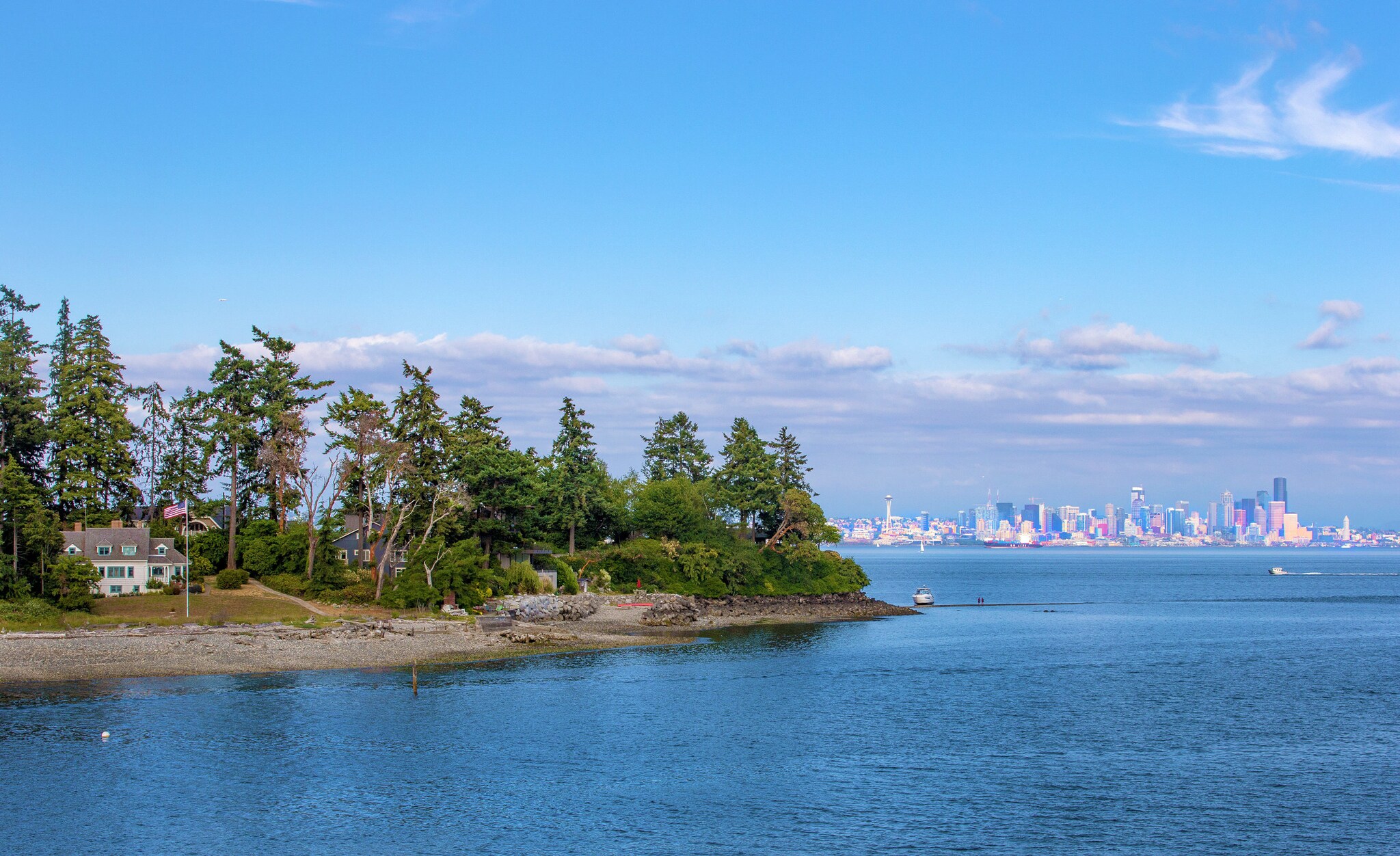 Vereinzelte Häuser auf einem schmalen Inselabschnitt, umgeben von Wasser vor Seattles Skyline im Hintergrund. Vereinzelte Häuser auf einem schmalen Inselabschnitt, umgeben von Wasser vor Seattles Skyline im Hintergrund.