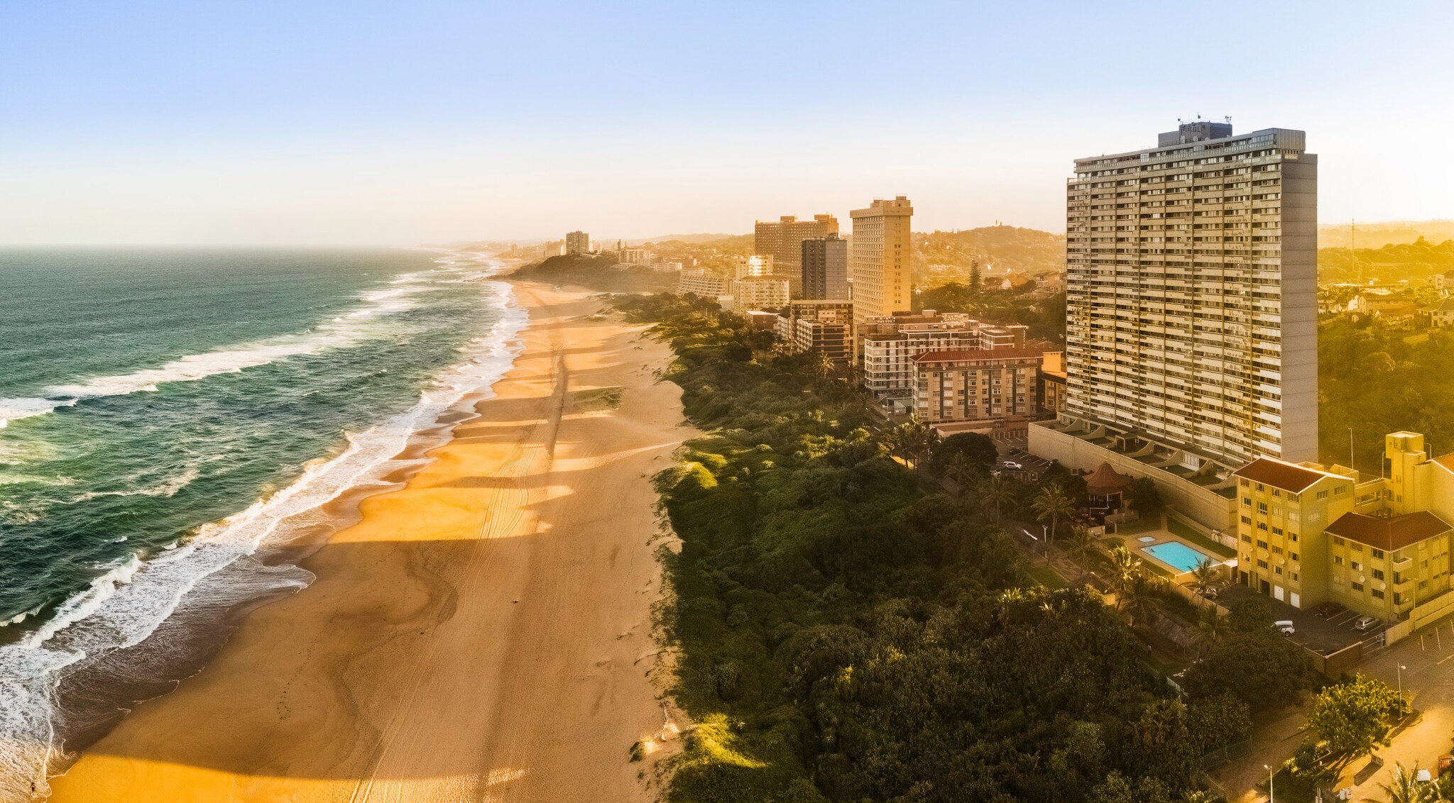 Ein breiter, langer Sandstrand an einer Küste mit großen Hotelbauten im goldenen Sonnenlicht. Ein breiter, langer Sandstrand an einer Küste mit großen Hotelbauten im goldenen Sonnenlicht.