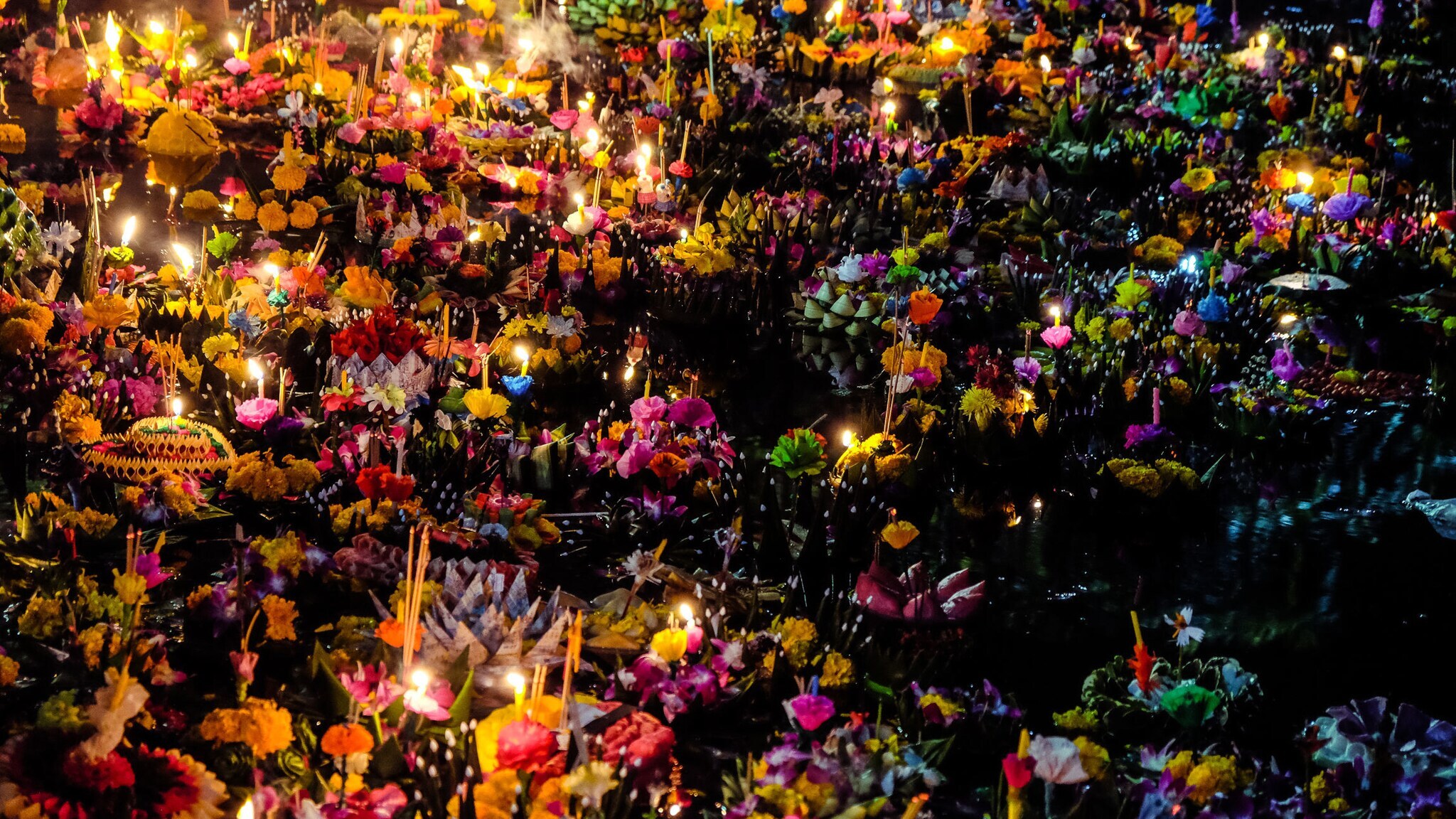 Kleine Flöße üppig geschmückt mit Blumen, Kerzen und Räucherstäbchen im Wasser im Dunkeln. Kleine Flöße üppig geschmückt mit Blumen, Kerzen und Räucherstäbchen im Wasser im Dunkeln.