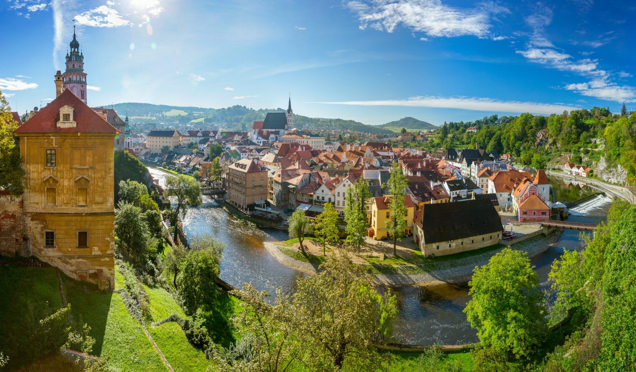 Mittelalterliche Kleinstadt mit Burg an einer Flussschlinge, umgeben von grünen Hügeln bei Sonnenschein.