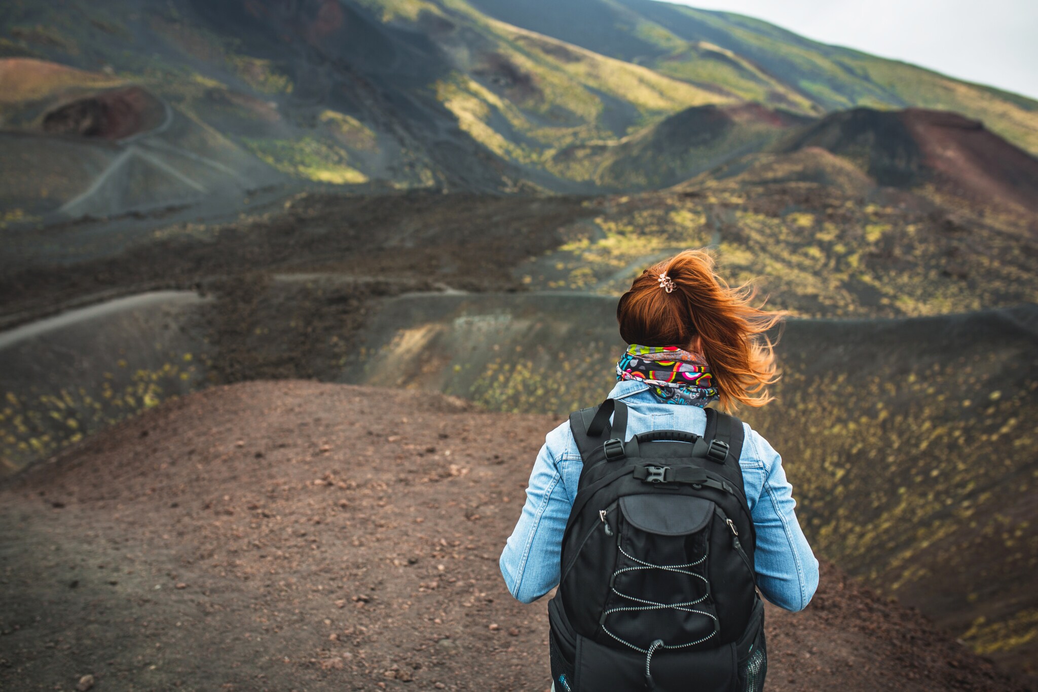 Eine Person von hinten mit einem Rucksack auf dem Rücken in einer braunen Vulkanlandschaft. Eine Person von hinten mit einem Rucksack auf dem Rücken in einer braunen Vulkanlandschaft.
