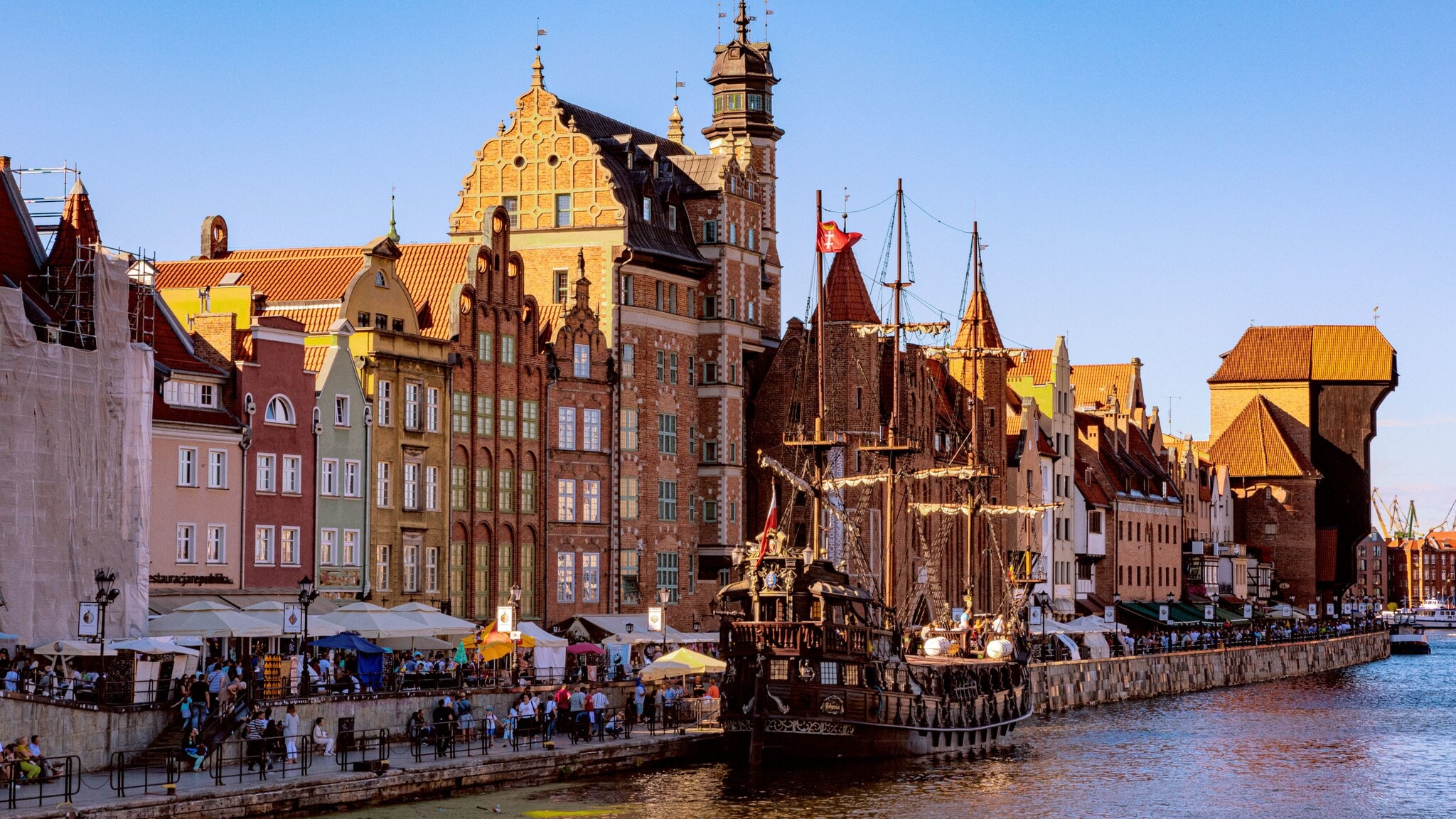 Personen an einer Uferpromenade mit den mittelalterlichen Handelshäusern und historischem Mastschiff. Personen an einer Uferpromenade mit den mittelalterlichen Handelshäusern und historischem Mastschiff.