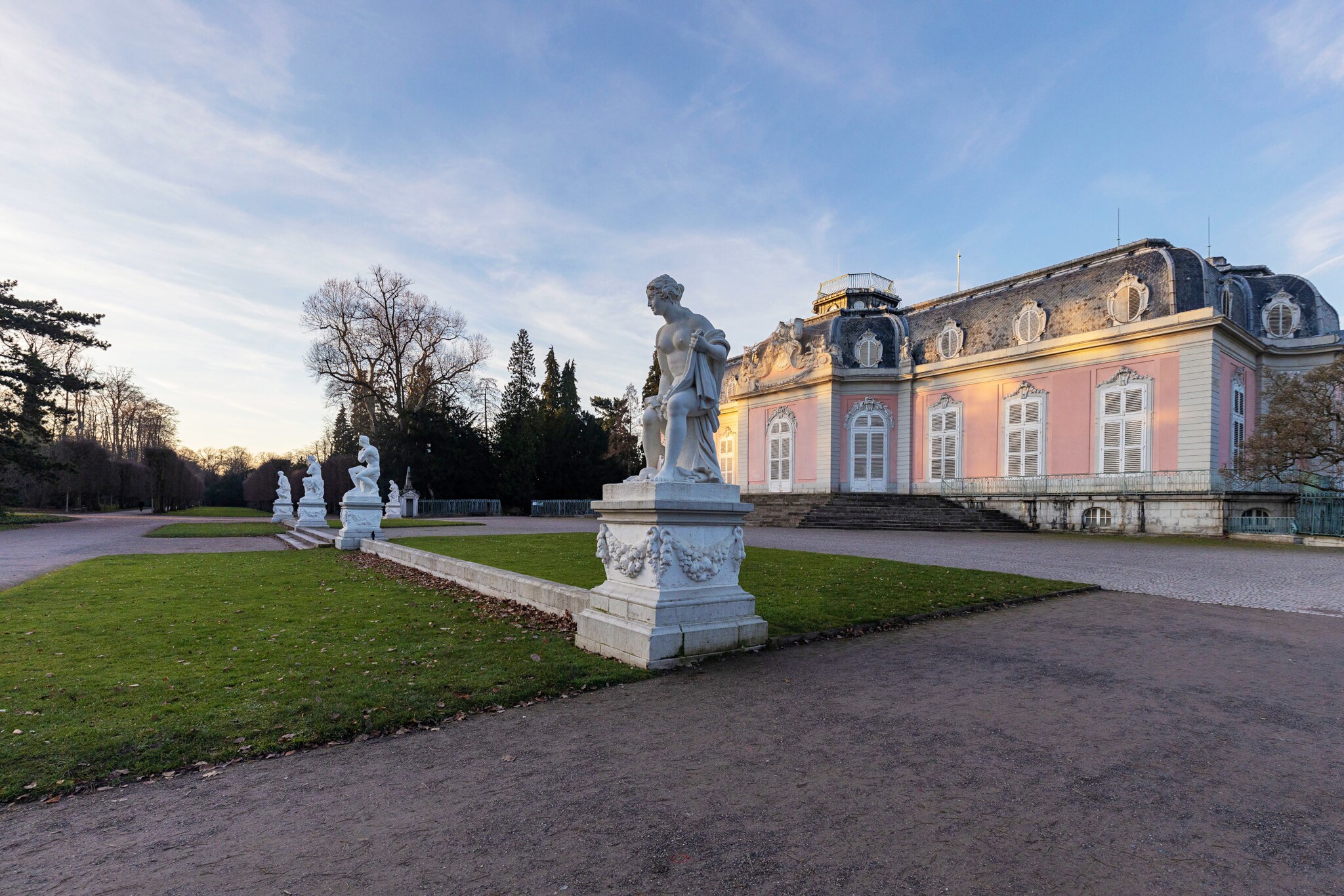 Rosafarbenes Schloss mit Steinskulpturen in einer Parkanlage im Vordergrund.
