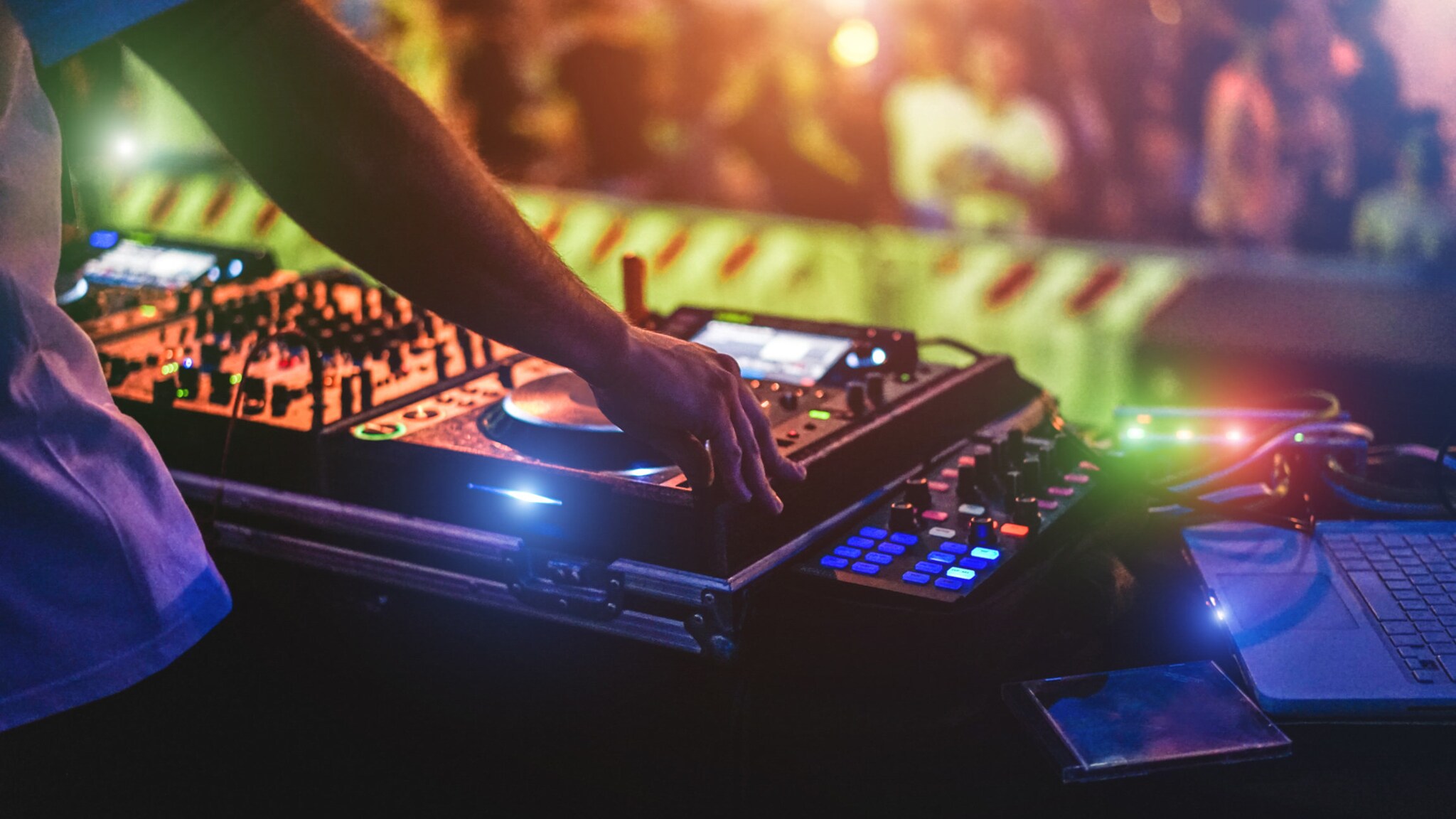 Eine unkenntliche Person, die an einem DJ Pult auf einer Bühne steht.