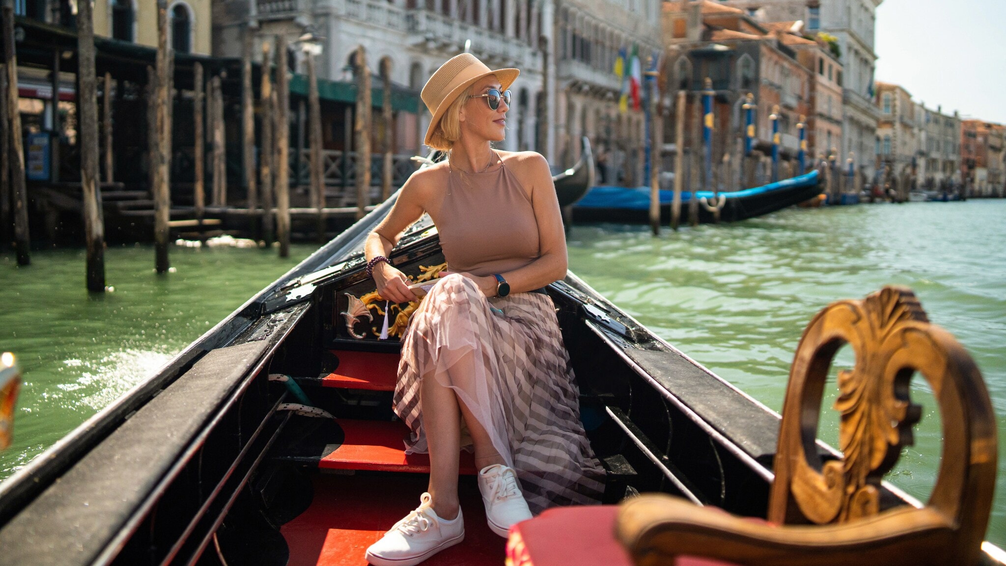 Eine Frau mit Sonnenbrille und Sonnenhut sitzt in einer Gondel auf einem Kanal in Venedig. Eine Frau mit Sonnenbrille und Sonnenhut sitzt in einer Gondel auf einem Kanal in Venedig.