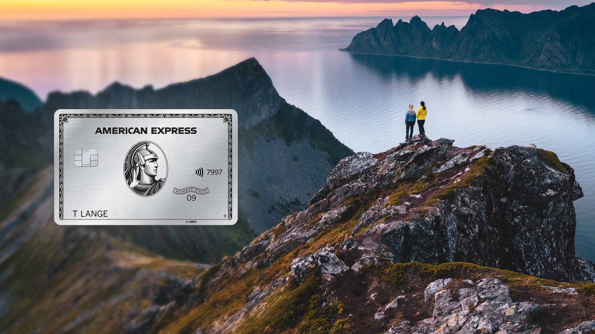 Zwei Personen stehen auf einem Felsen in einer kargen Berglandschaft am Wasser bei Sonnenuntergang. Zwei Personen stehen auf einem Felsen in einer kargen Berglandschaft am Wasser bei Sonnenuntergang.