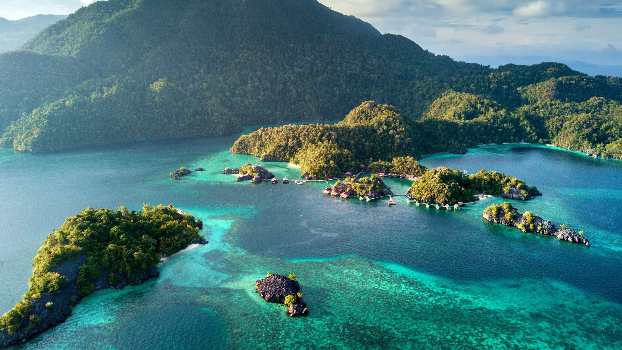 Luftaufnahme einer tropischen Inselgruppe mit bewaldeten Hügeln, umgeben von türkisblauem Wasser. Luftaufnahme einer tropischen Inselgruppe mit bewaldeten Hügeln, umgeben von türkisblauem Wasser.