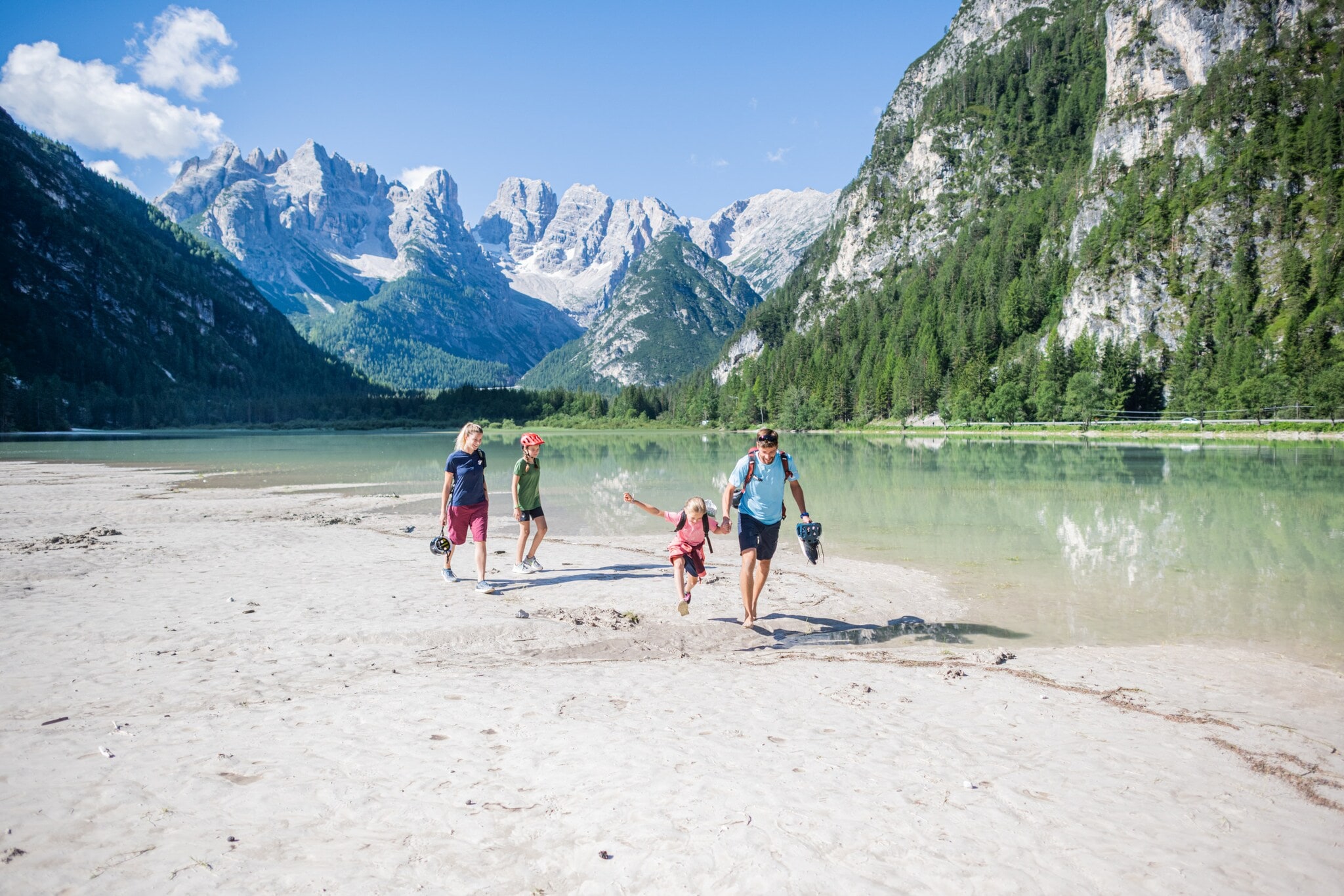 Eine Familie mit zwei Kindern in sommerlicher Sportkleidung läuft an einem See in den Bergen entlang. Eine Familie mit zwei Kindern in sommerlicher Sportkleidung läuft an einem See in den Bergen entlang.