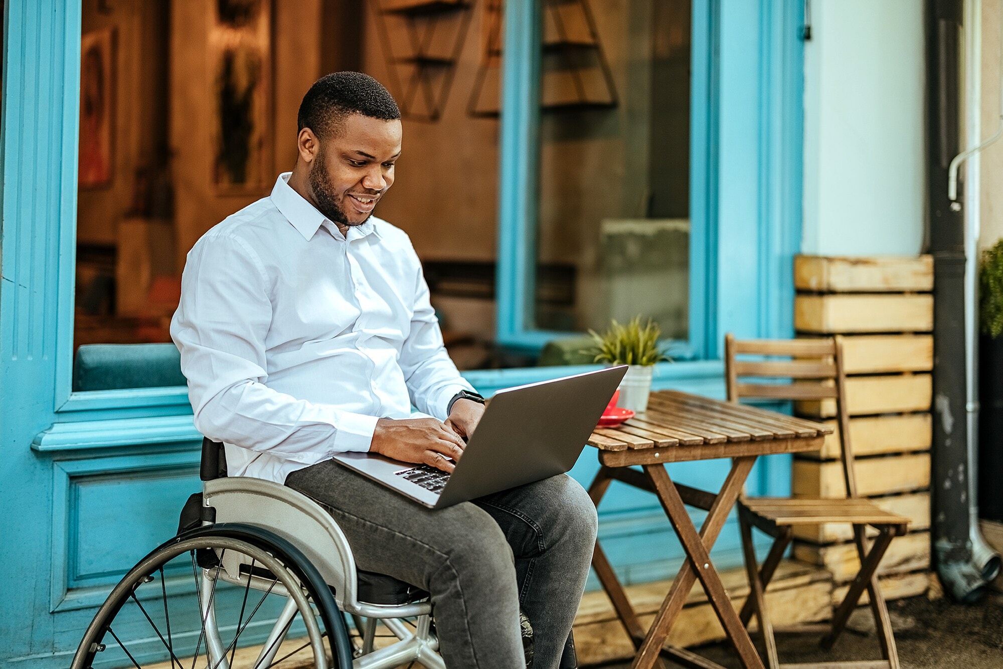 Work-Life-Blending: Ein Erfolgsmodell mit Zukunft Ein junger Mann im Rollstuhl arbeitet am Laptop auf der Terrasse eines Cafés.