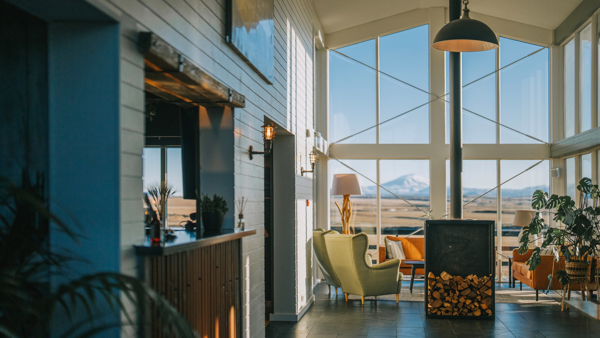 Foyer eines stylishen Hotels mit Holzofen und Blick auf eine weitläufige Landschaft mit schneebedecktem Vulkan.
