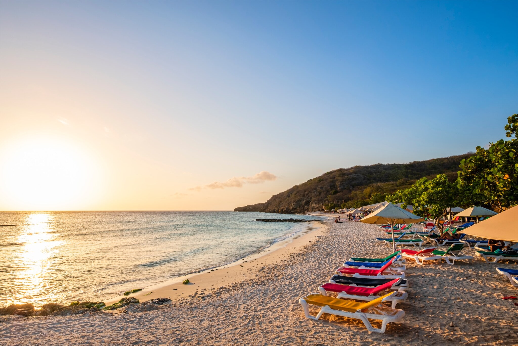 Strand bei Sonnenuntergang mit bunten Liegen und Sonnenschirmen. Strand bei Sonnenuntergang mit bunten Liegen und Sonnenschirmen.