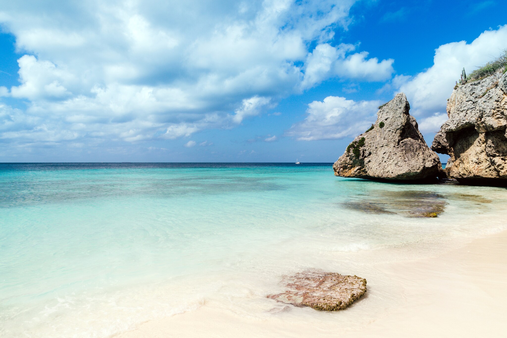 Weißer Strand am türkisblauen Meer, am Rand große Felsen im Wasser.