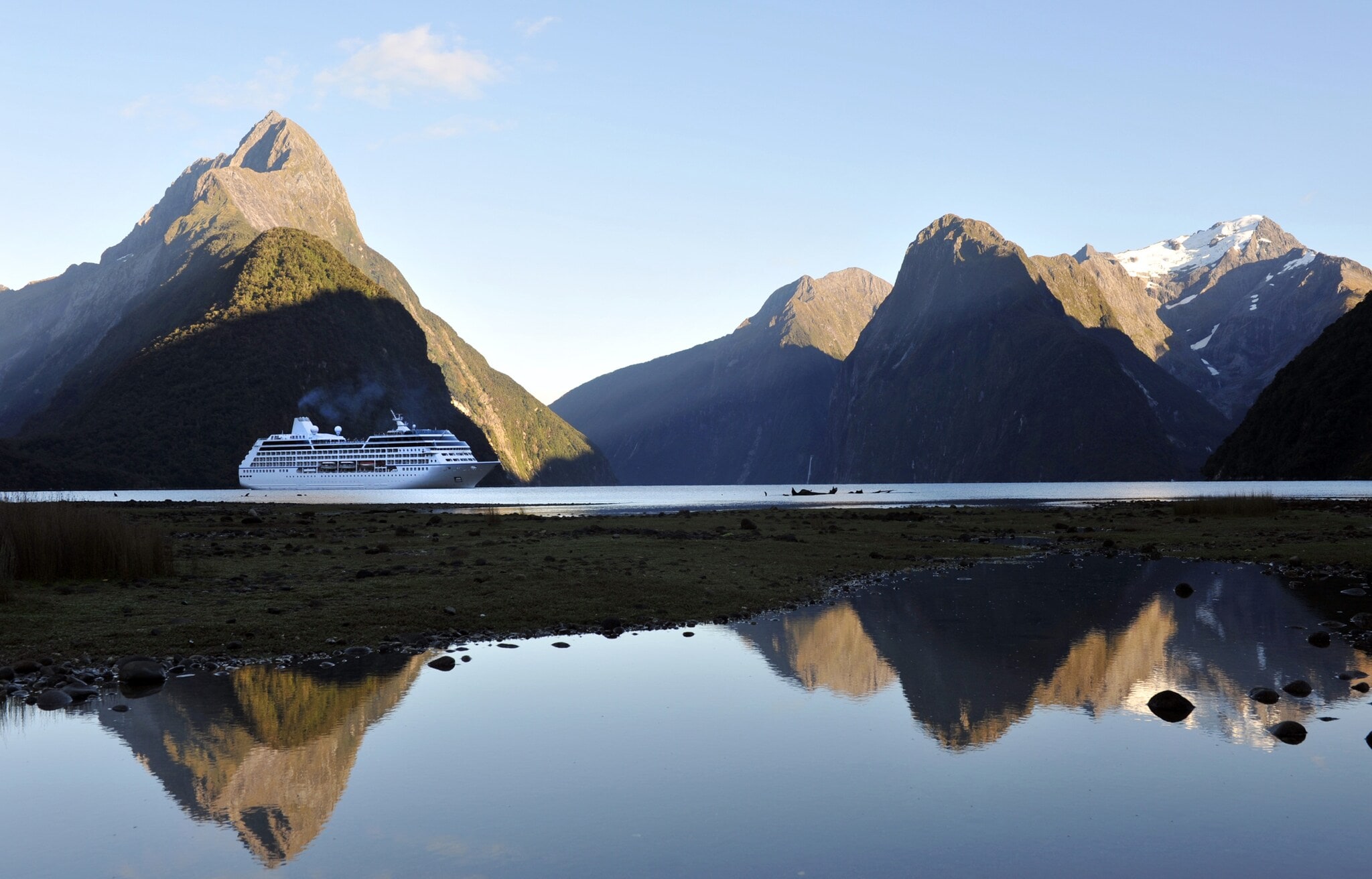 Ein Kreuzfahrtschiff durchquert den Milford Sound in Neuseeland, während sich die hügelige Landschaft des Hintergrunds im ruhigen Wasser spiegelt.