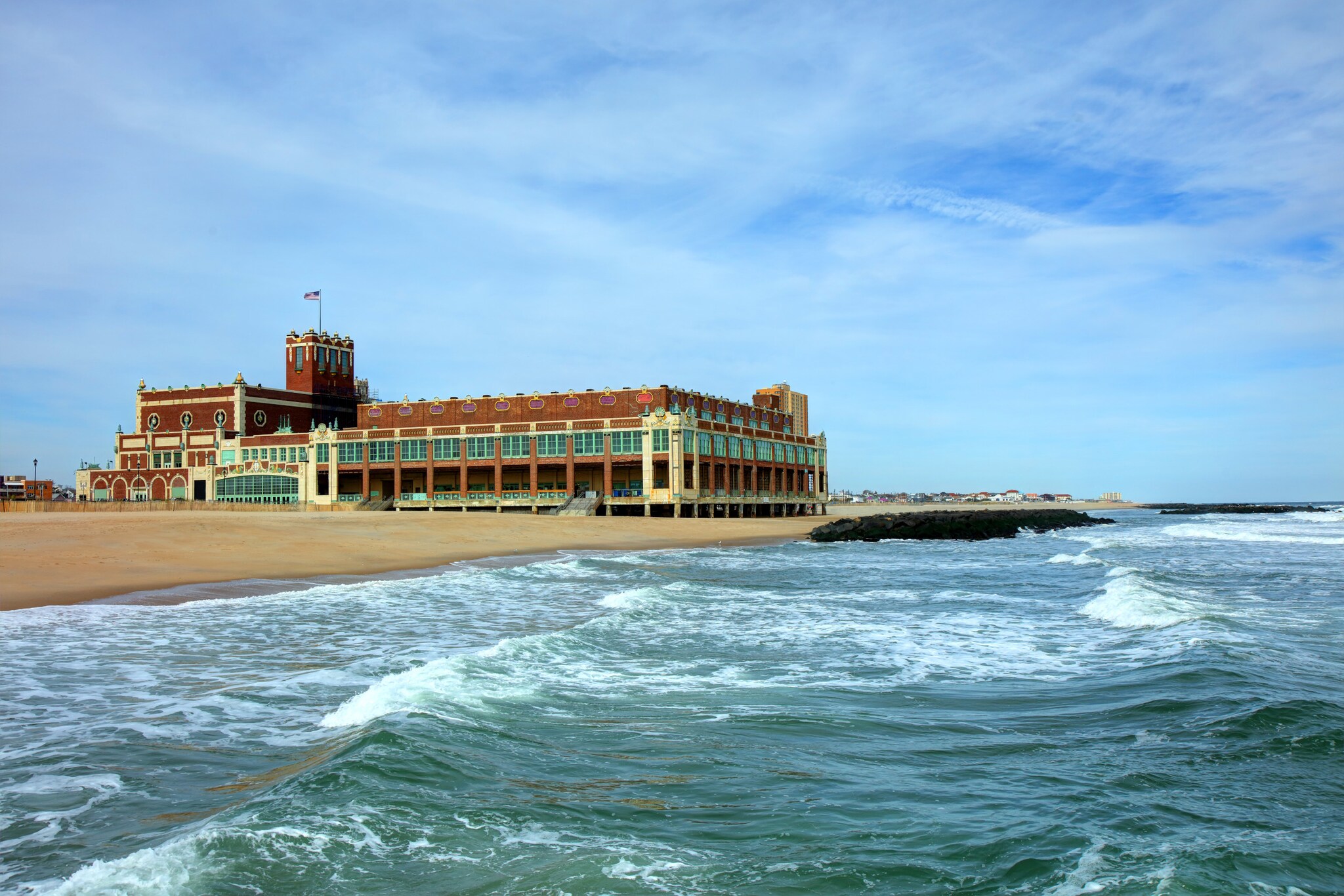 Blick vom Wasser auf ein großes Gebäude mit US-Flagge an einem Sandstrand.