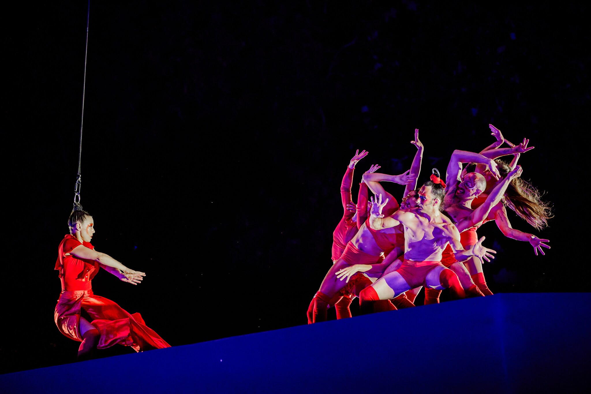 Eine Artistin im roten Kleid an einem Seil vor einer tanzenden Gruppe. Eine Artistin im roten Kleid an einem Seil vor einer tanzenden Gruppe.