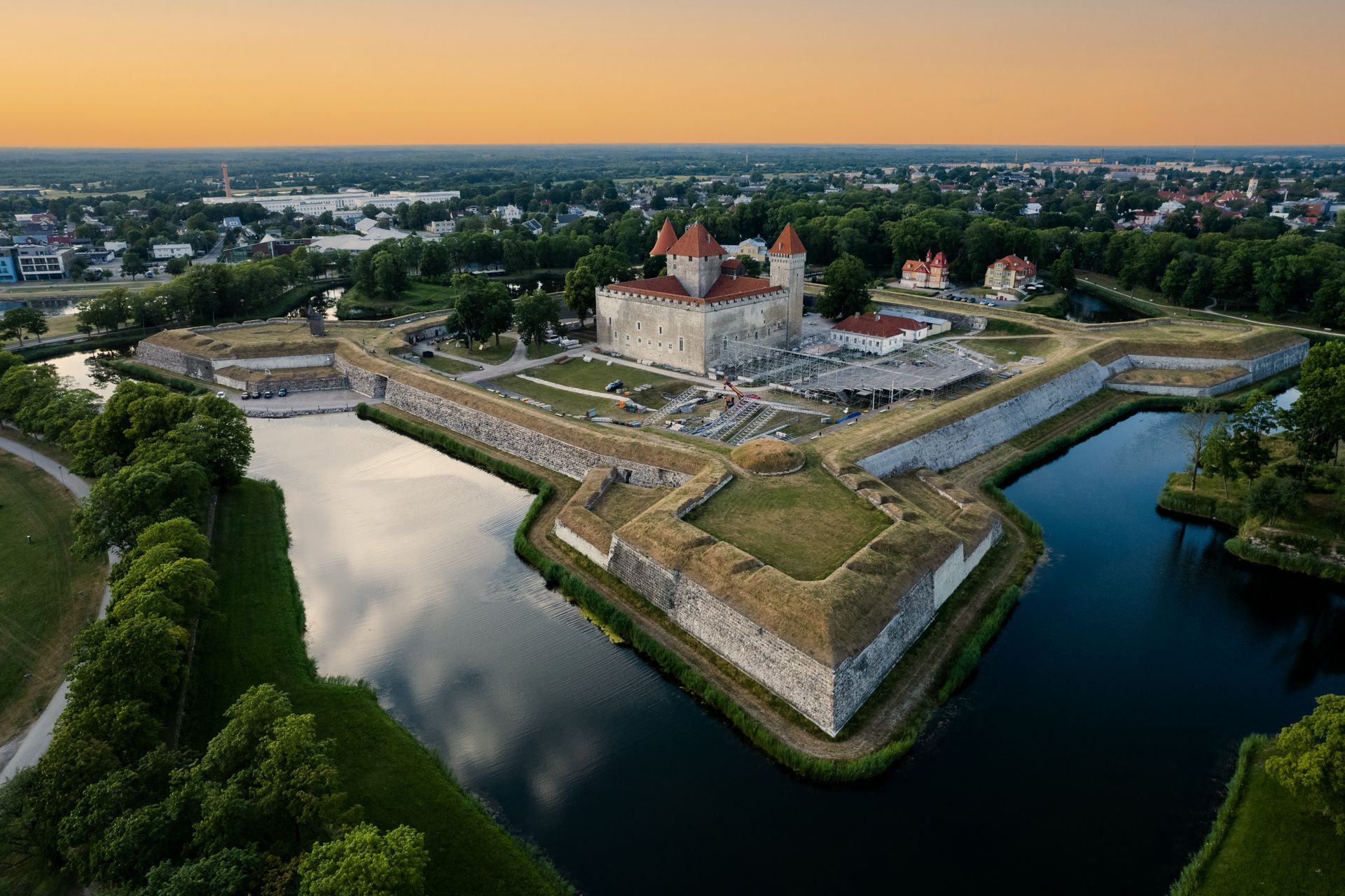 Eine helle Burg mit roten Dächern, umgeben von einem mit Wasser gefüllten Burggraben.