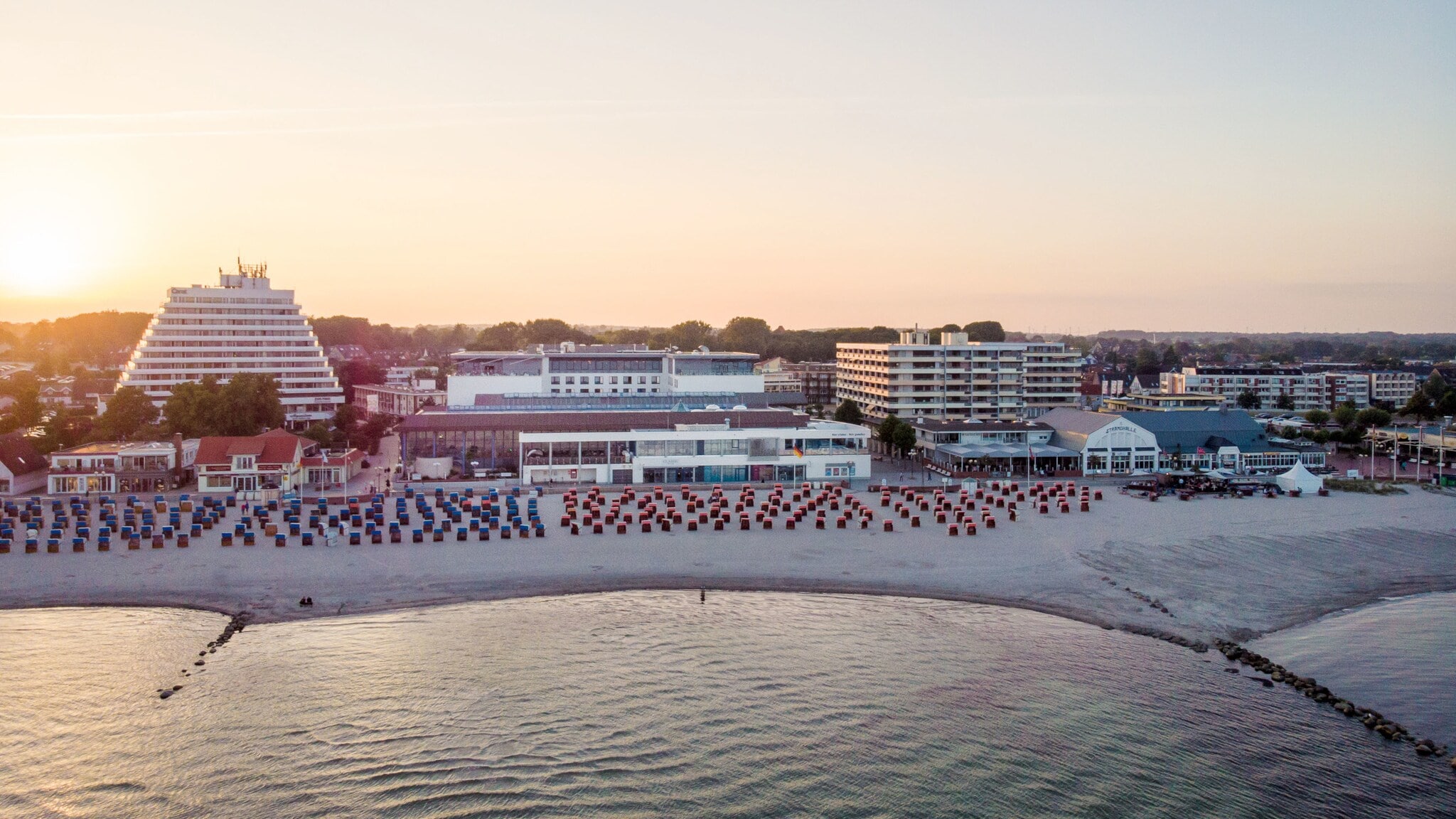 Luftaufnahme eines Hotelkomplexes mit Sandstrand am Meer bei Abenddämmerung.