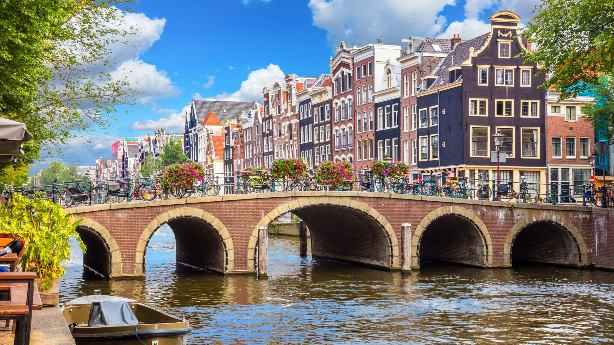 Eine mit Blumen geschmückte Steinbrücke über einem Kanal vor einer Reihe Grachtenhäuser im Stadtzentrum von Amsterdam.