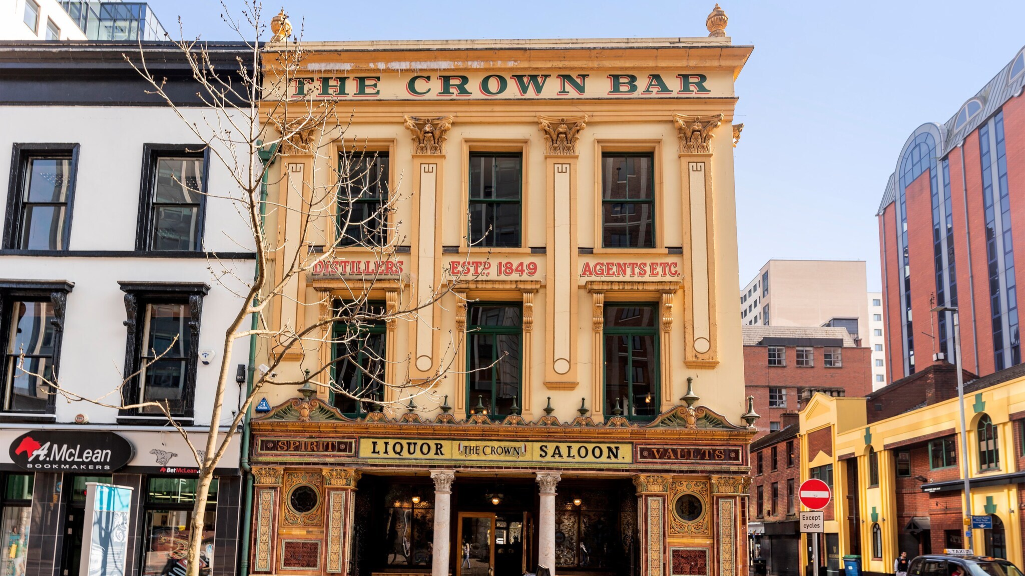 Fassade der historischen Kneipe 'The Crown Bar' mit goldener Verzierung und Schildern wie 'Liquor Saloon' in einer Stadtstraße