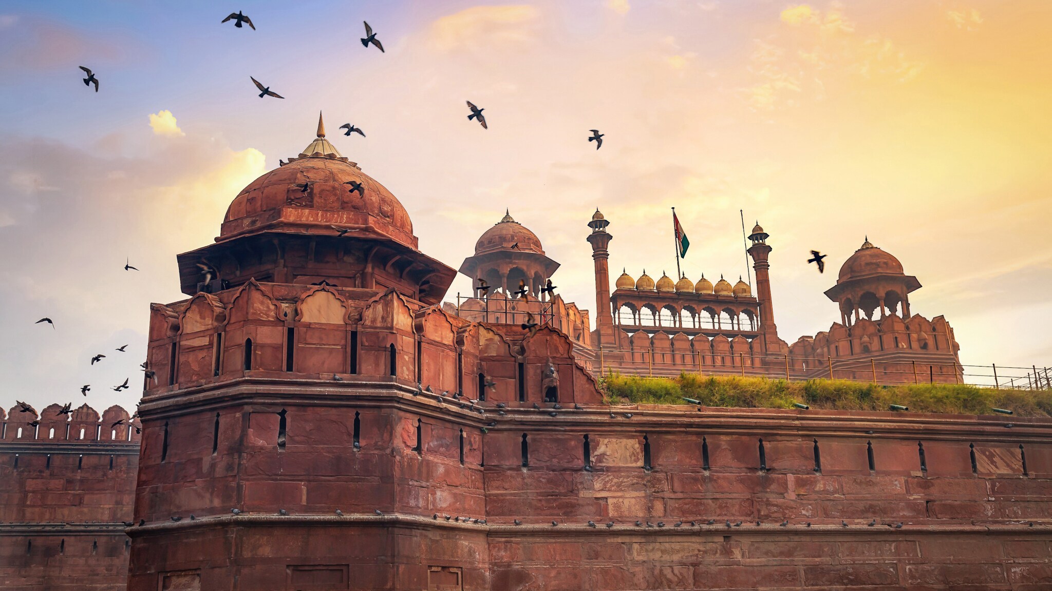 Rotes Fort in Indien bei Sonnenuntergang mit fliegenden Vögeln am Himmel Rotes Fort in Indien bei Sonnenuntergang mit fliegenden Vögeln am Himmel
