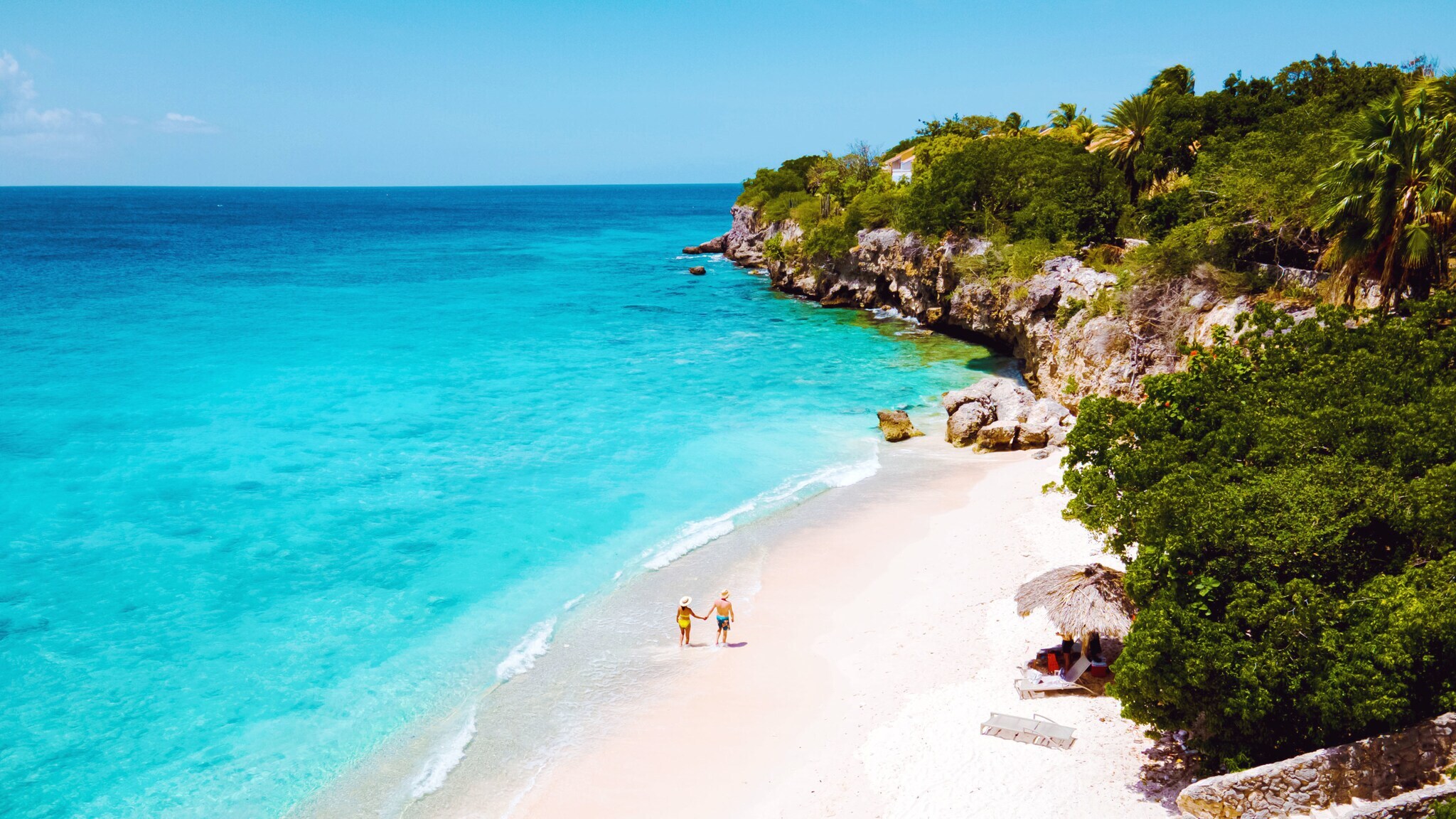Zwei Personen auf einem weißen Sandstrand an türkisblauem Meer in einer Felsbucht mit grüner Vegetation. Zwei Personen auf einem weißen Sandstrand an türkisblauem Meer in einer Felsbucht mit grüner Vegetation.