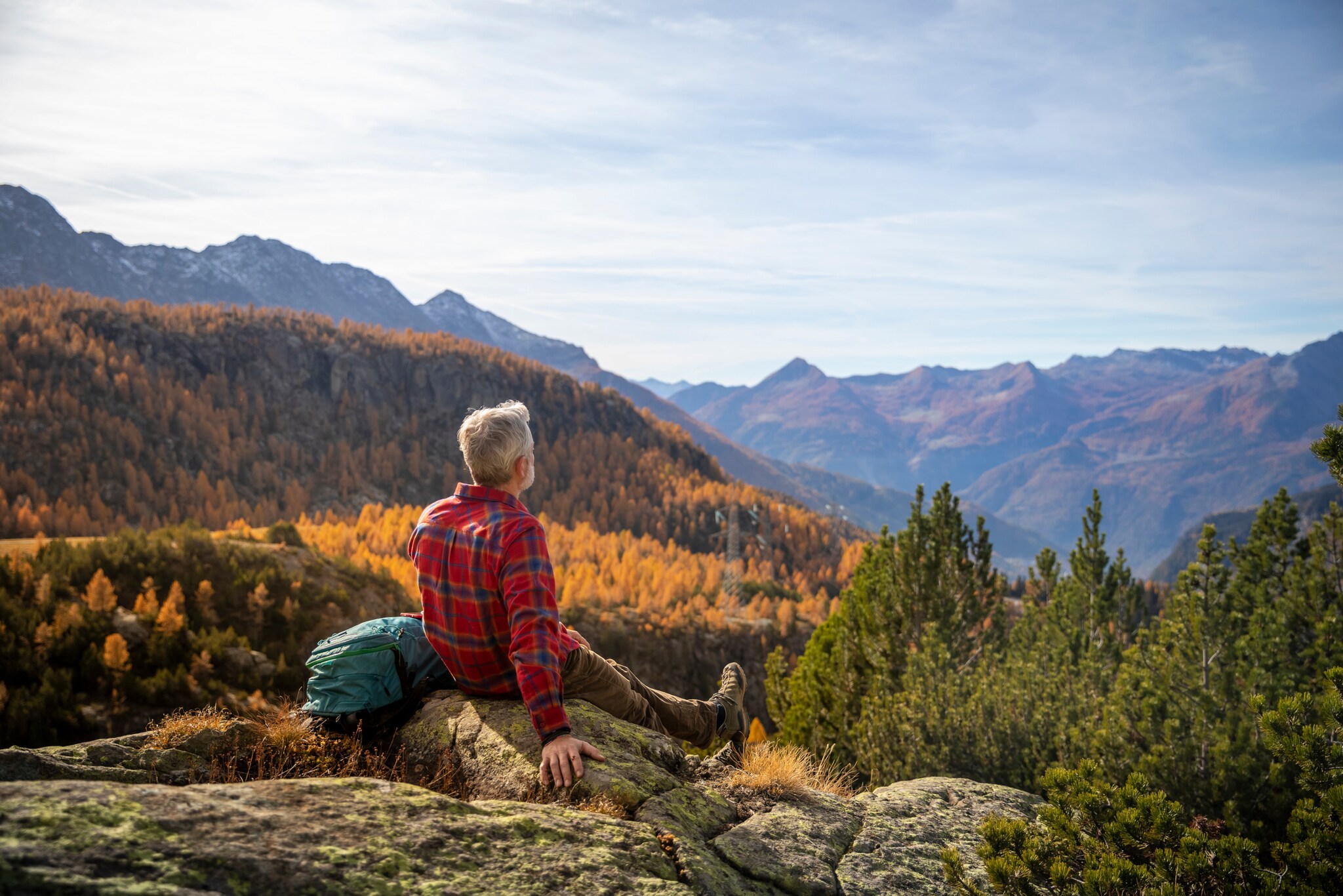 Ein Mann sitzt auf einem Berg und blickt auf farbenprächtige Bäume. Ein Mann sitzt auf einem Berg und blickt auf farbenprächtige Bäume.