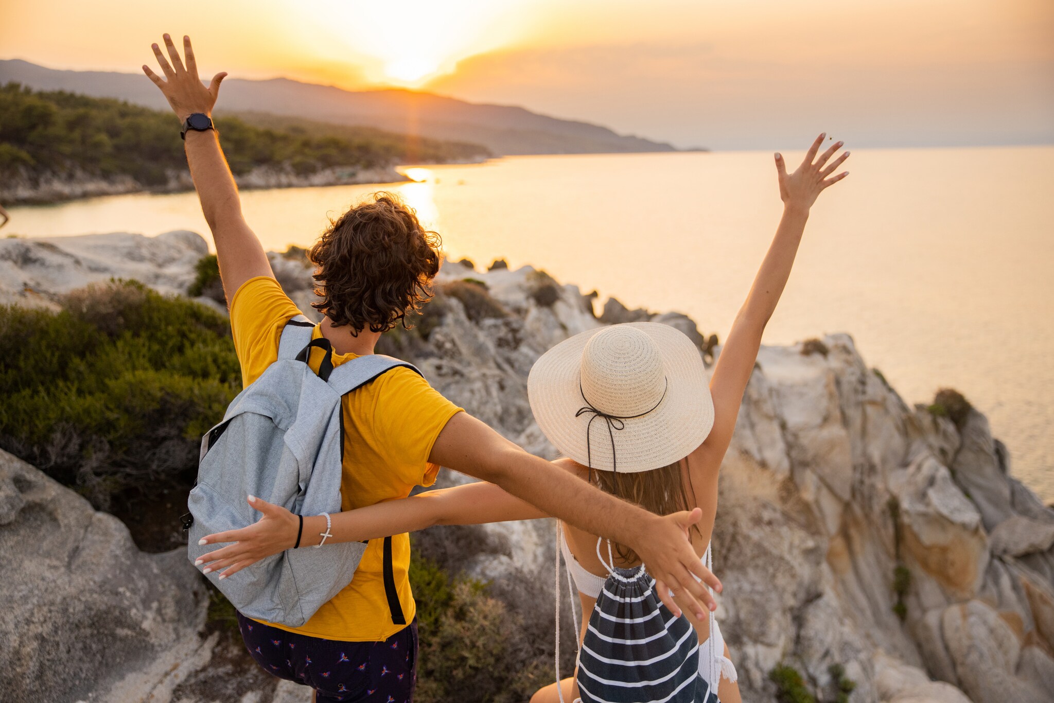 Ein Paar steht mit offenen Armen auf einem Felsen und schaut auf das Meer und den Sonnenuntergang. Ein Paar steht mit offenen Armen auf einem Felsen und schaut auf das Meer und den Sonnenuntergang.