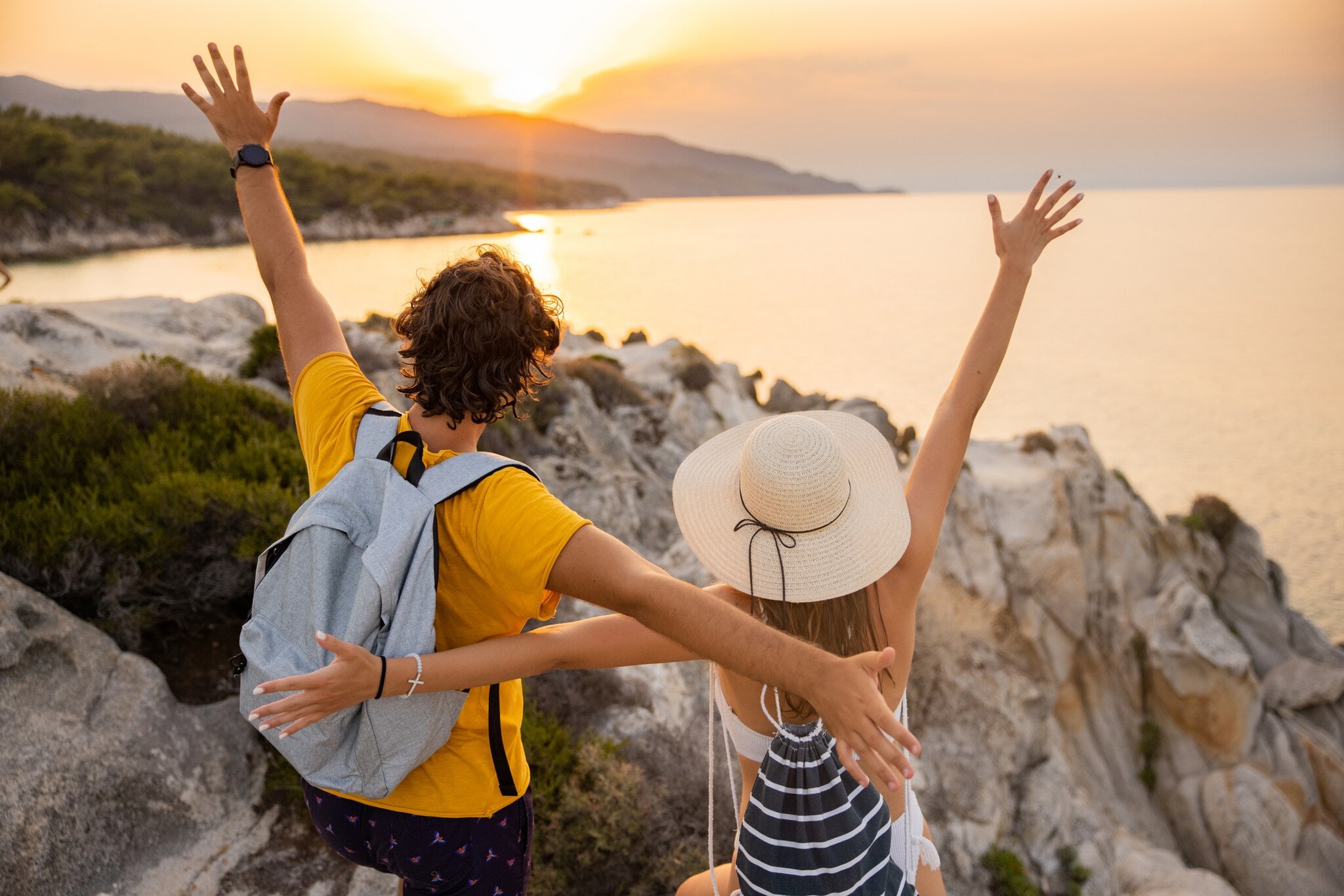 Ein Paar steht mit offenen Armen auf einem Felsen und schaut auf das Meer und den Sonnenuntergang. Ein Paar steht mit offenen Armen auf einem Felsen und schaut auf das Meer und den Sonnenuntergang.