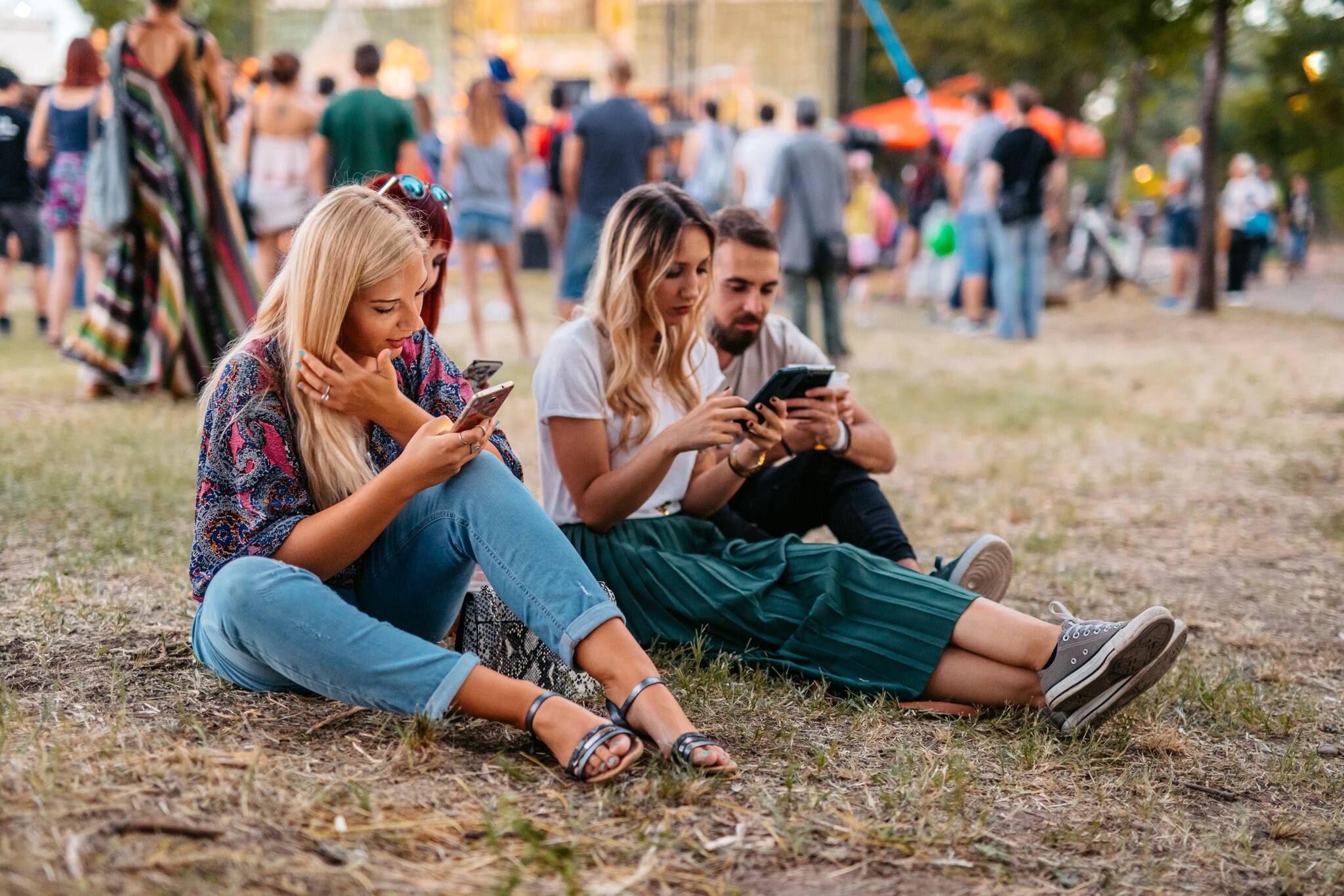Freunde sitzen im Gras bei einem Festival und schauen auf ihre Smartphones. Freunde sitzen im Gras bei einem Festival und schauen auf ihre Smartphones.