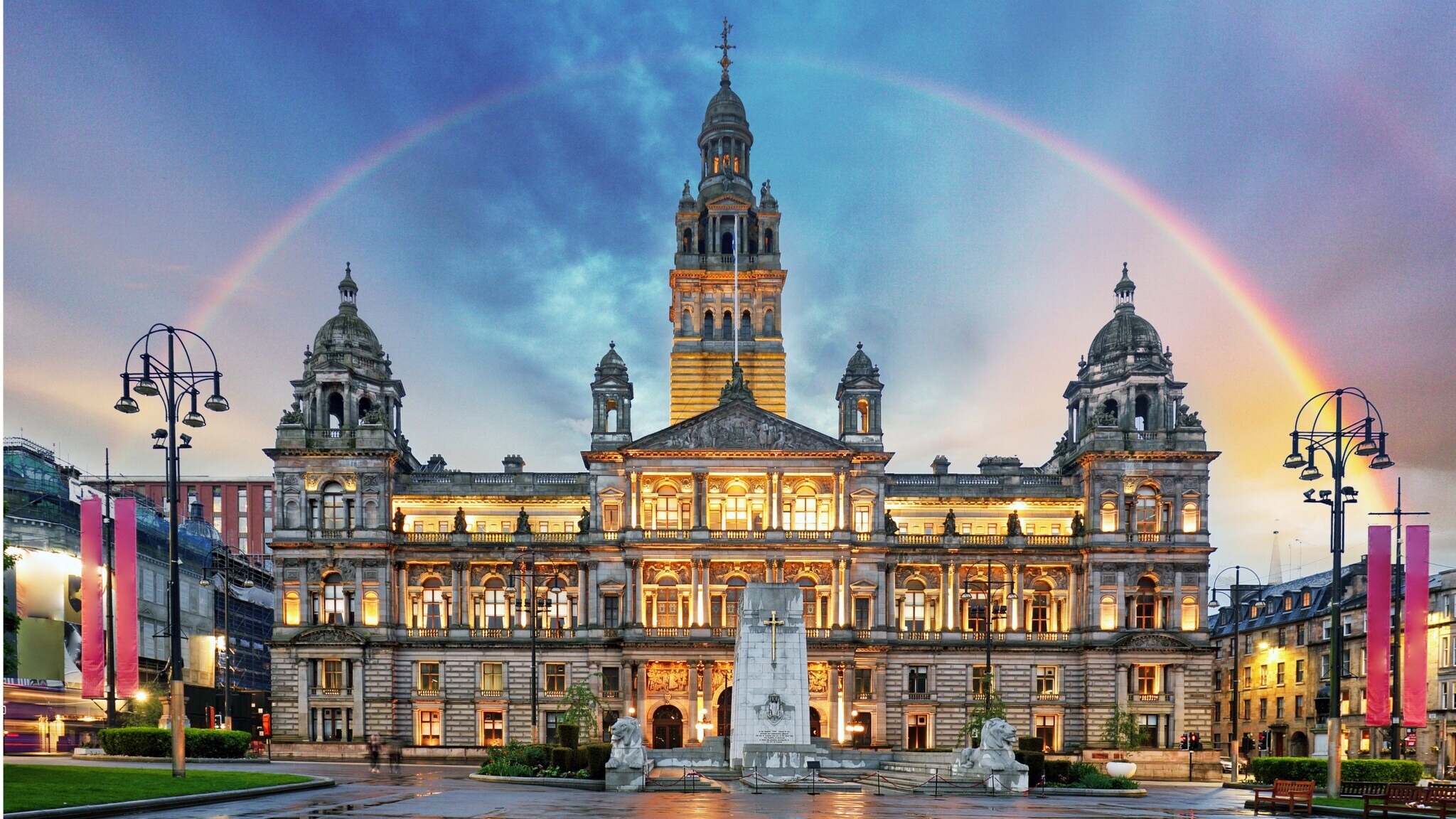 Beleuchtetes historisches Rathausgebäude bei Dämmerung mit Regenbogen am Himmel Beleuchtetes historisches Rathausgebäude bei Dämmerung mit Regenbogen am Himmel