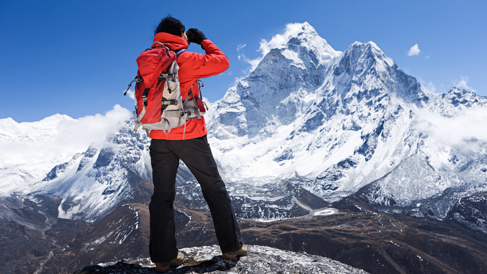 Ein Wanderer in roter Jacke blickt auf einen schneebedeckten Berggipfel im Himalaja Ein Wanderer in roter Jacke blickt auf einen schneebedeckten Berggipfel im Himalaja