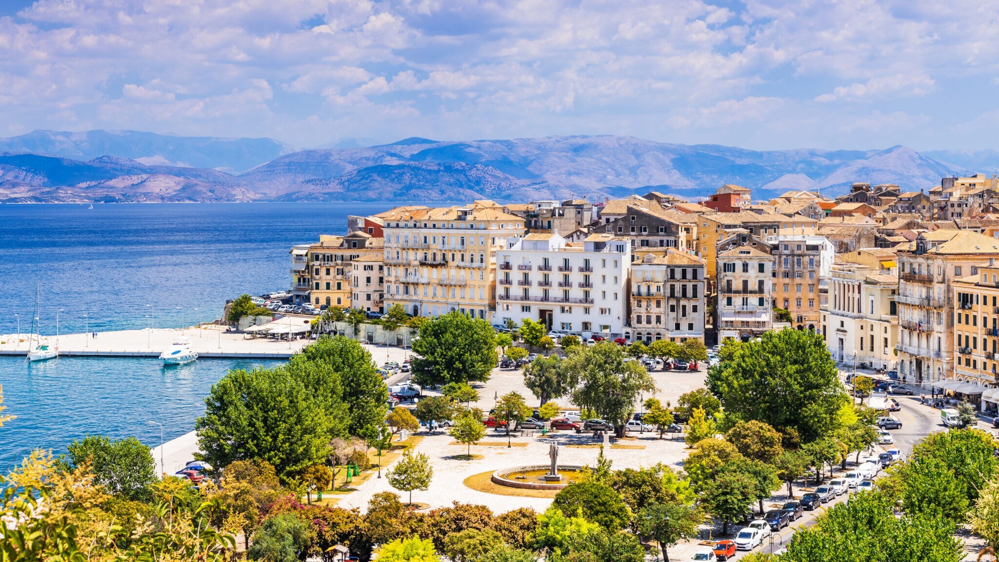 Küstenstadt mit historischen Gebäuden, Blick auf das blaue Meer und Berge im Hintergrund unter bewölktem Himmel Küstenstadt mit historischen Gebäuden, Blick auf das blaue Meer und Berge im Hintergrund unter bewölktem Himmel