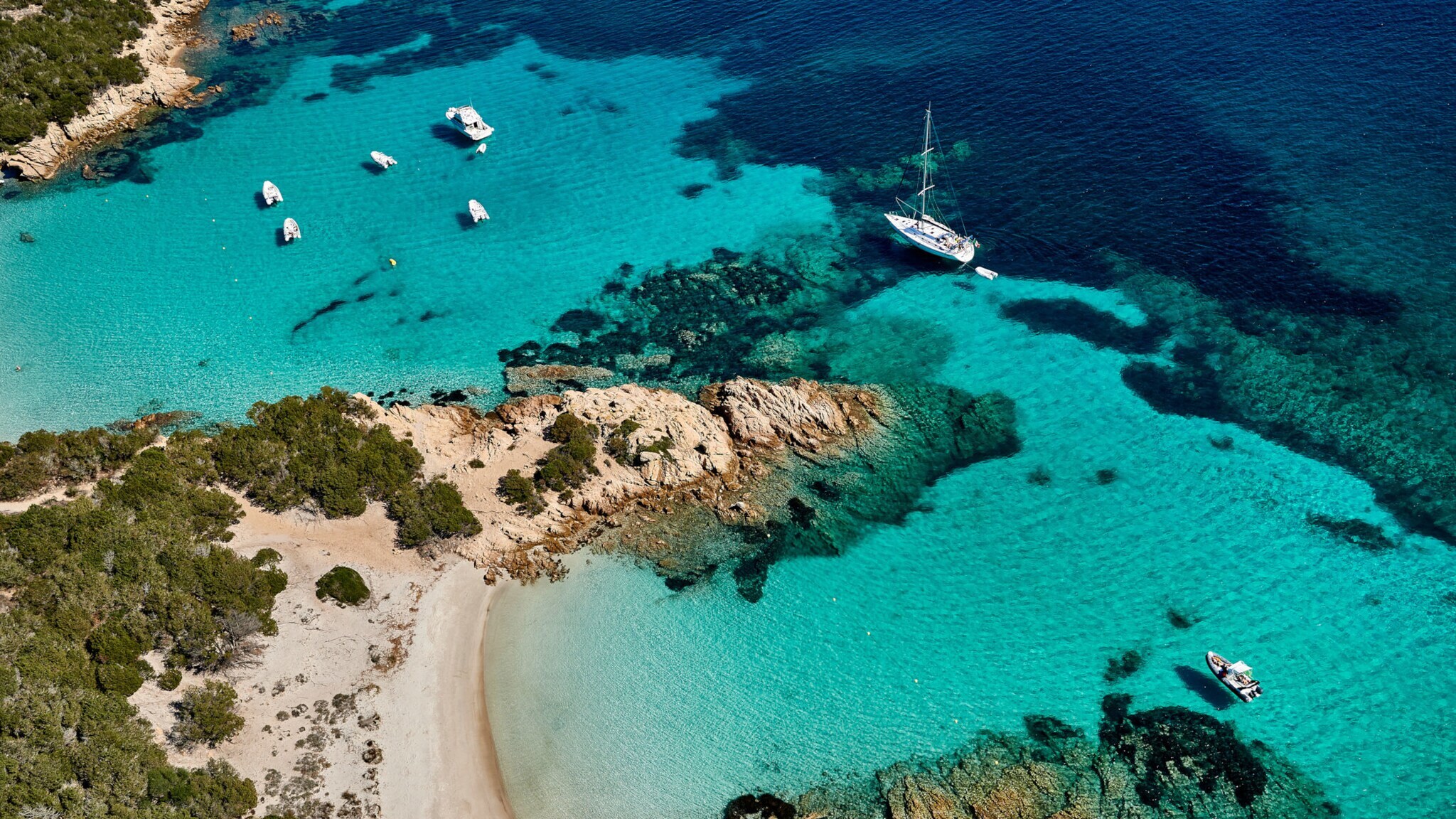 Aufsicht einer flachen Felsküste mit feinen Sandstränden an türkisblauem Meer mit Motorbooten.