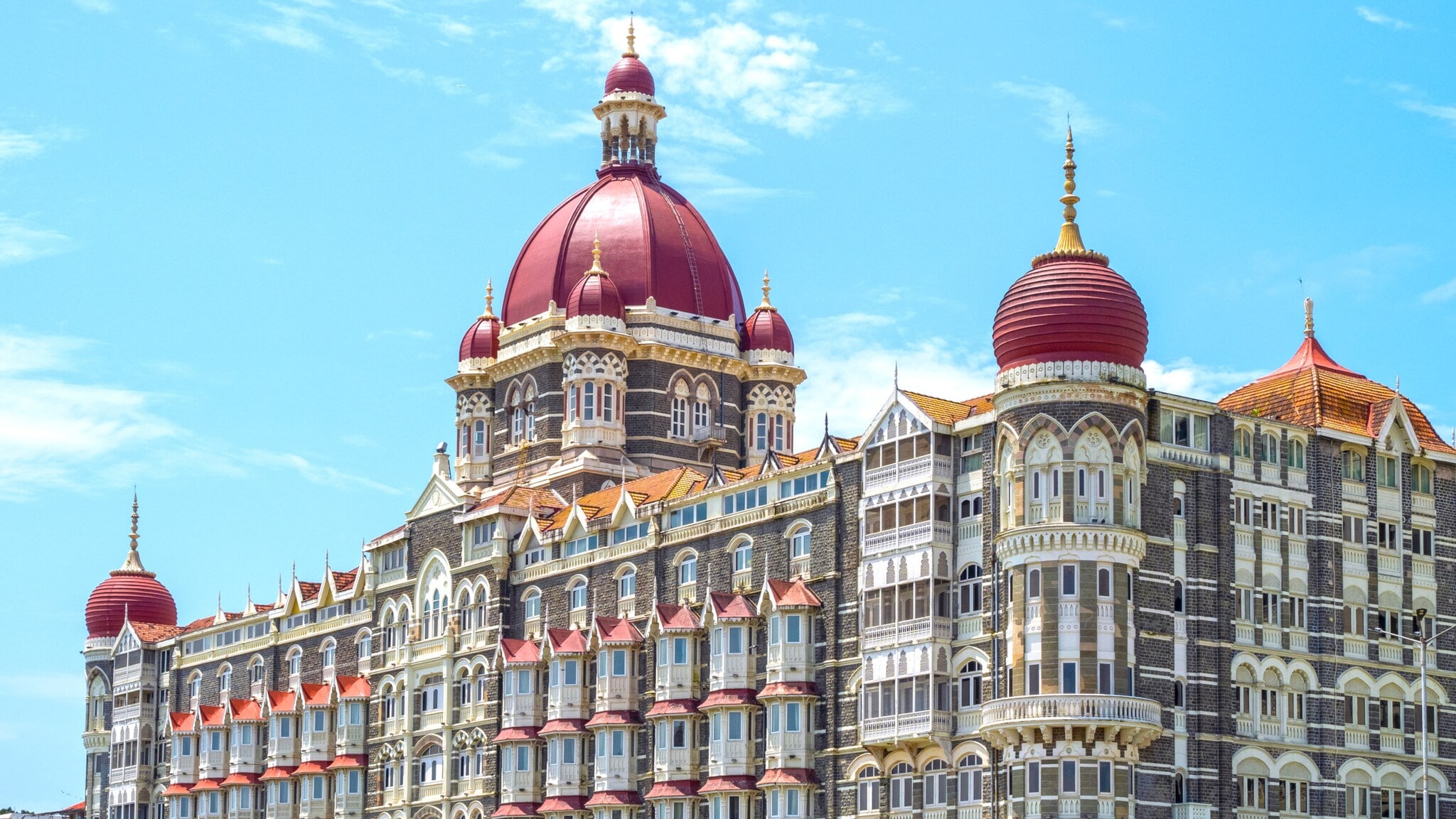Historisches Hotel Taj Mahal Palace in Mumbai mit roten Kuppeln und detailreicher Fassade unter blauem Himmel. Historisches Hotel Taj Mahal Palace in Mumbai mit roten Kuppeln und detailreicher Fassade unter blauem Himmel.
