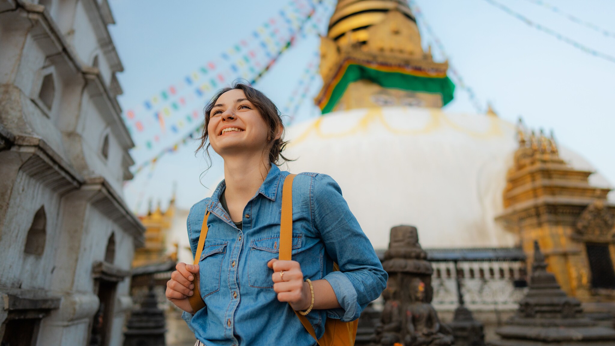 Eine junge, lächelnde Frau mit Rucksack vor einem nepalesischen Tempel.