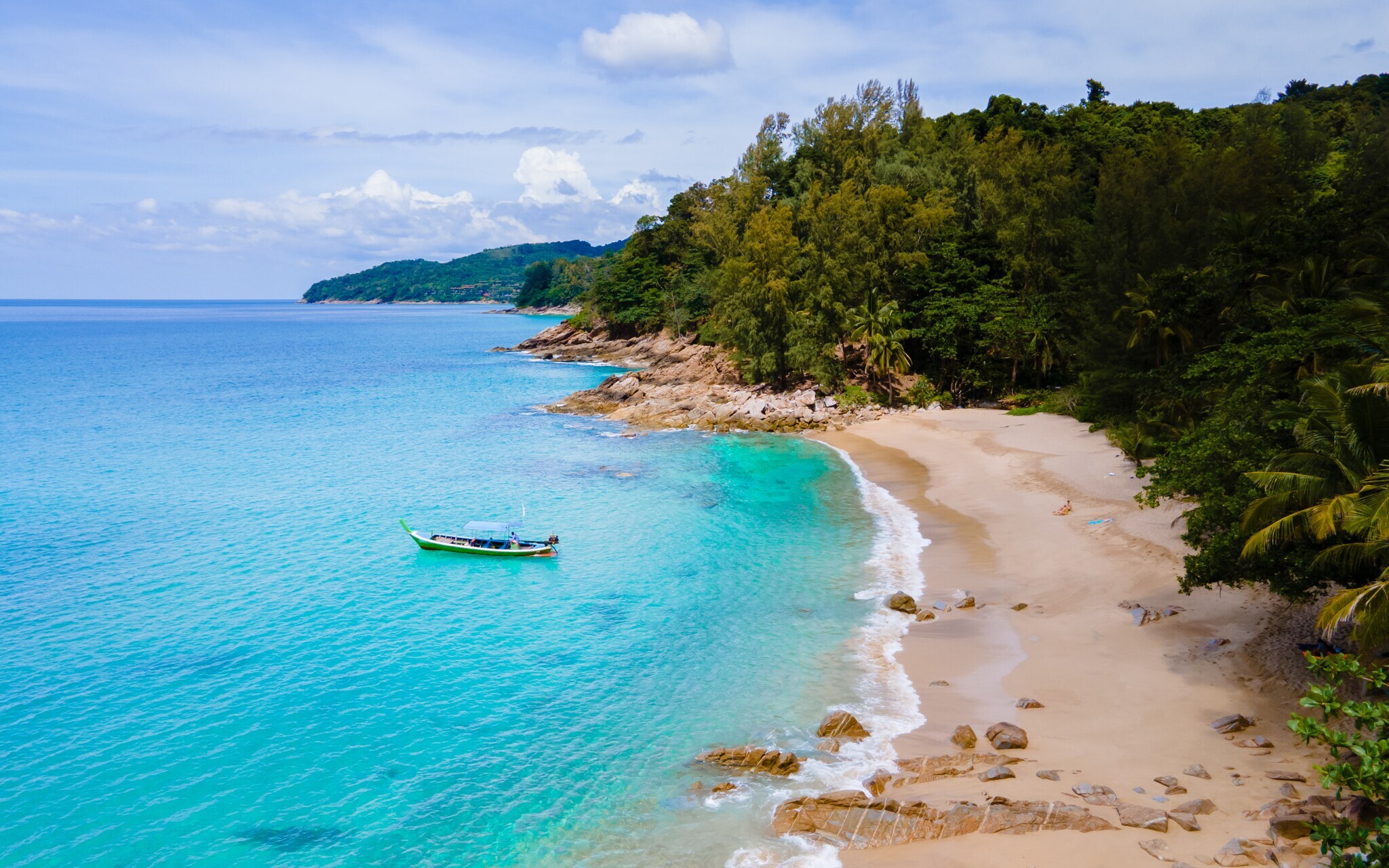 Kleine Meeresbucht mit einem Fischerboot im türkisblauen Wasser an einem Sandstrand, umgeben von tropischem Regenwald.