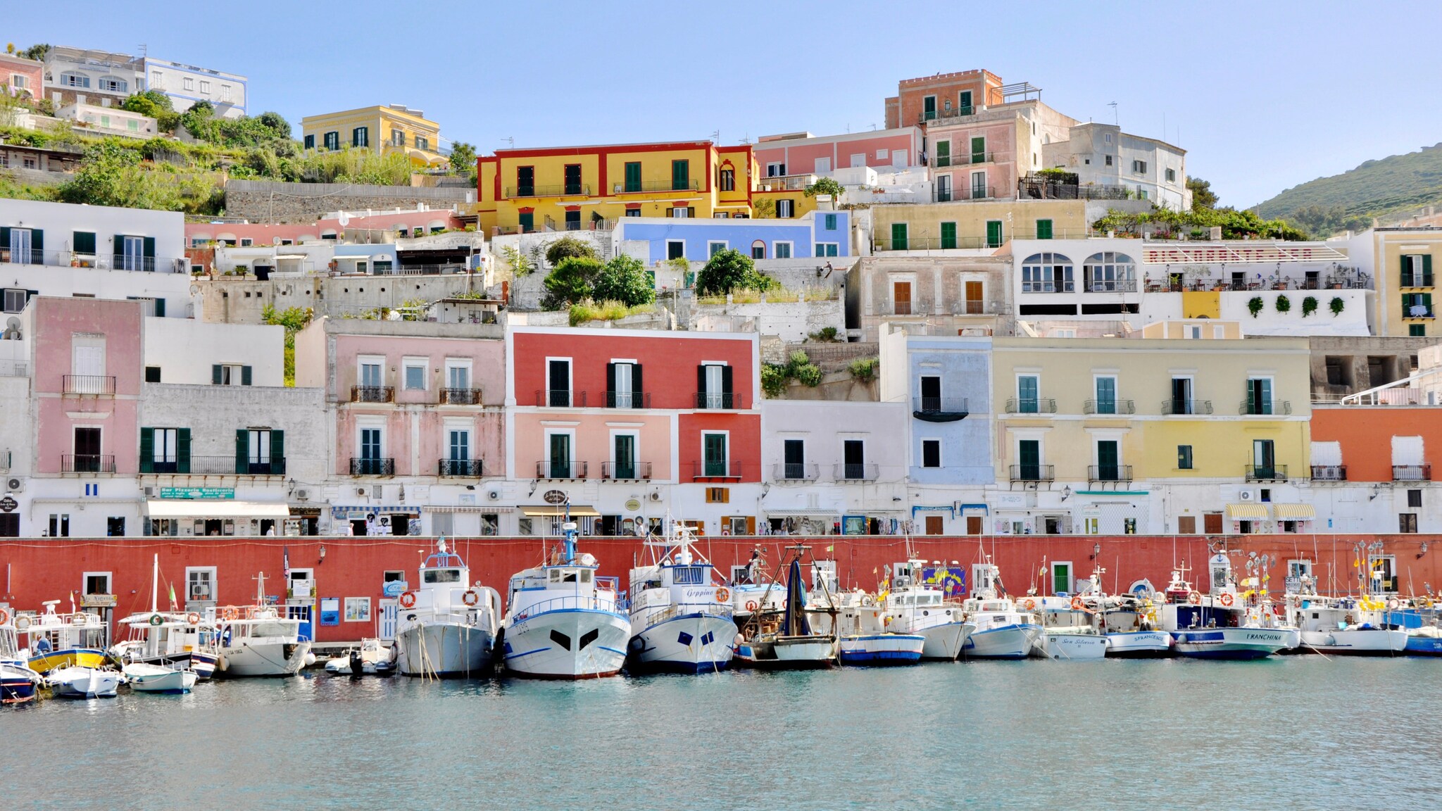 Bunte Häuser an einem Hang über dem Hafen von Ponza mit mehreren Booten im Wasser