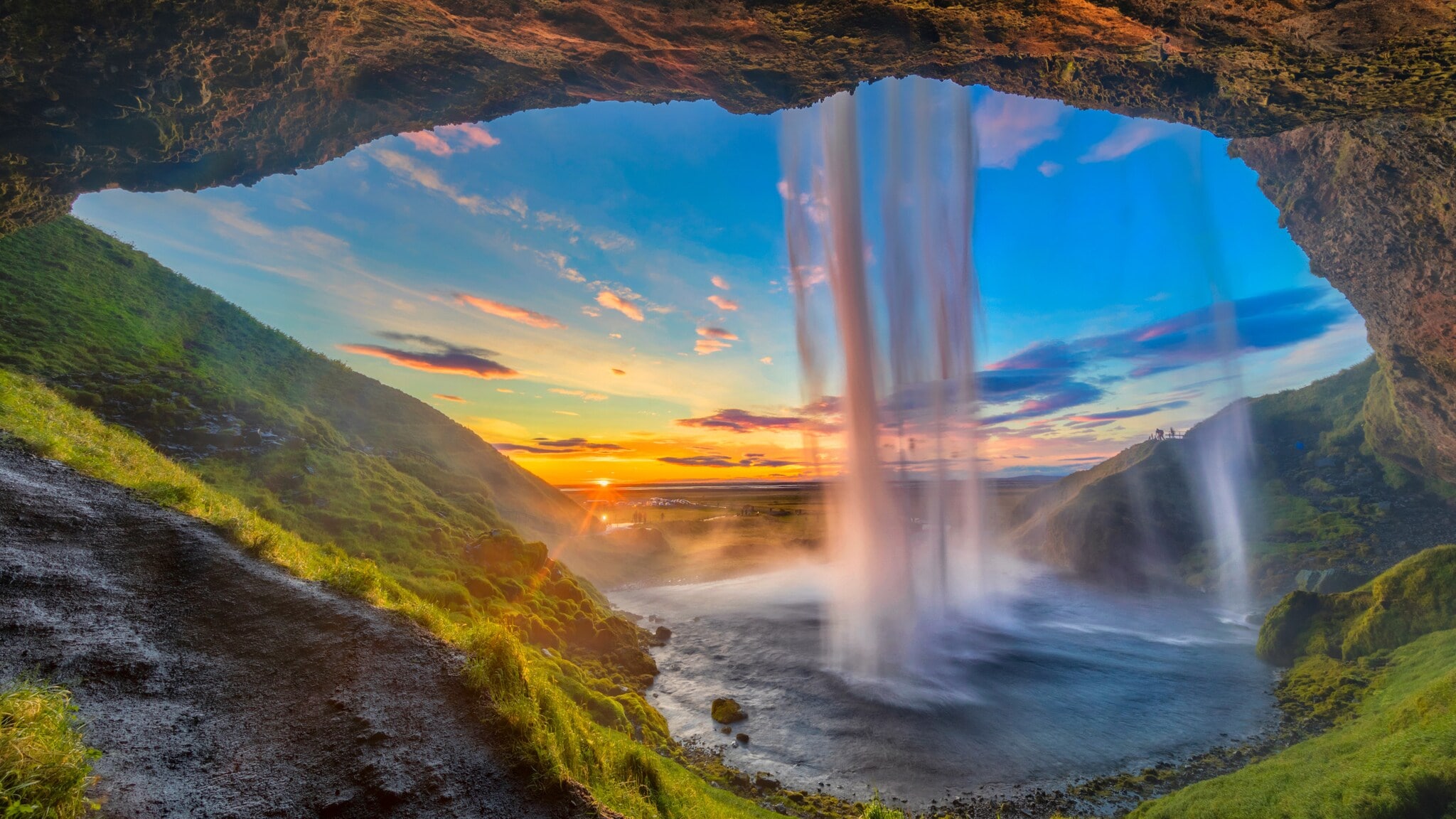 Wasserfall, der von einer Höhle aus bei Sonnenuntergang in eine grüne Landschaft fällt Wasserfall, der von einer Höhle aus bei Sonnenuntergang in eine grüne Landschaft fällt