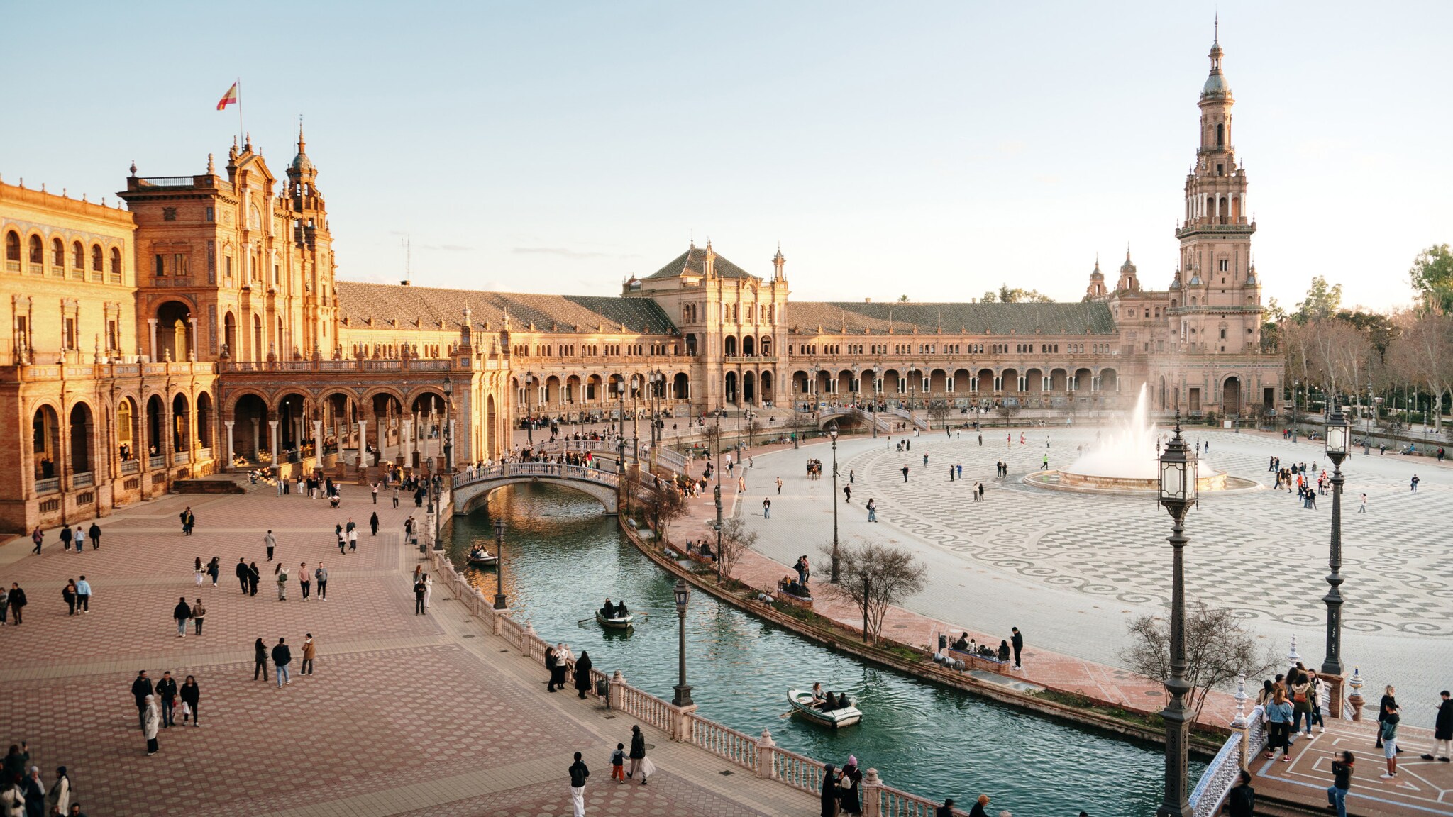 Plaza de España in Sevilla mit halbkreisförmigem Gebäude, Brücke über Kanal und zentralem Springbrunnen bei Tageslicht