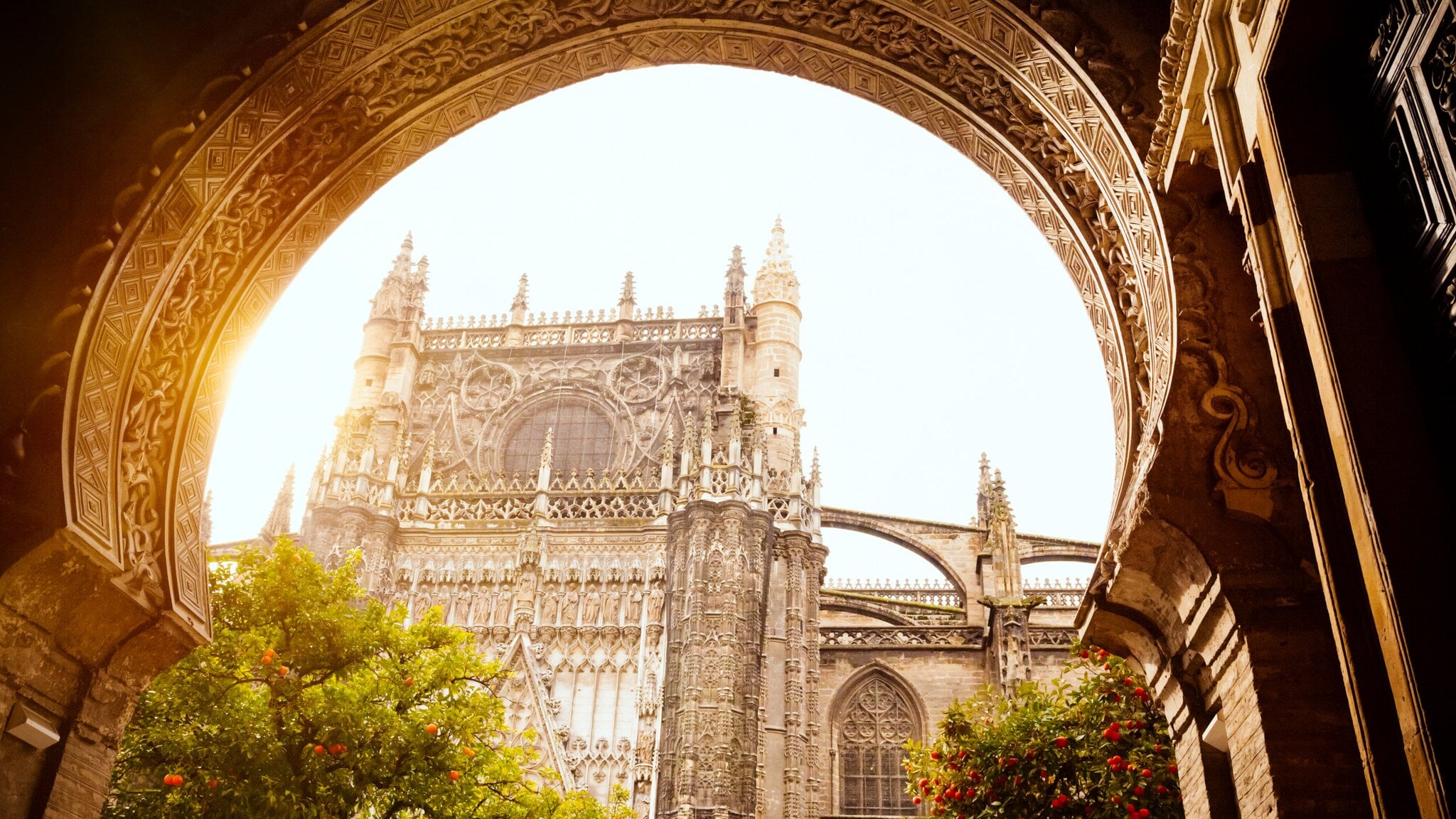 Gotische Kathedrale mit detaillierten Steinmetzarbeiten, gesehen durch einen verzierten Bogenrahmen bei Sonnenlicht Gotische Kathedrale mit detaillierten Steinmetzarbeiten, gesehen durch einen verzierten Bogenrahmen bei Sonnenlicht