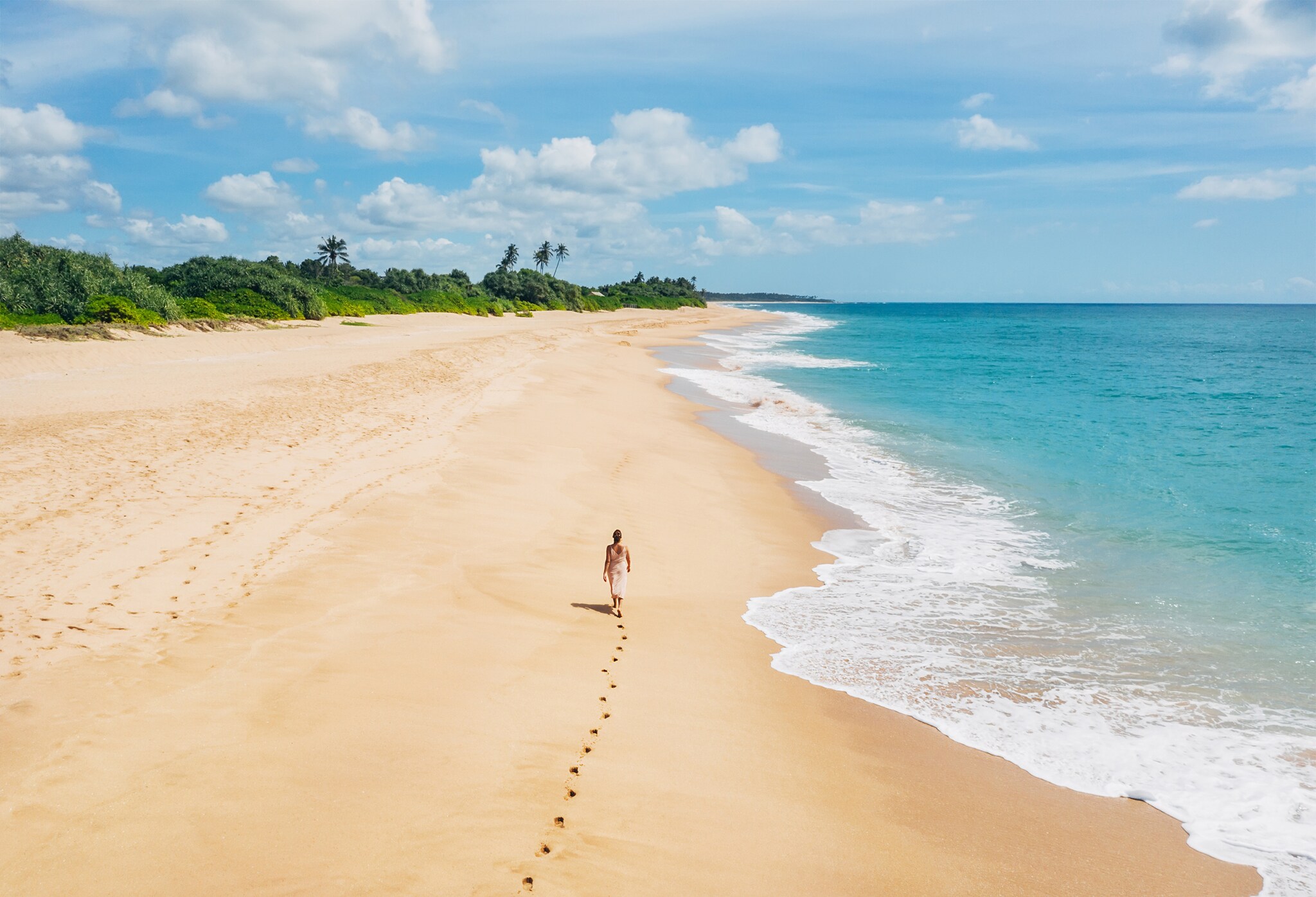 Rückansicht einer Frau, die einen breiten Sandstrand entlangläuft.